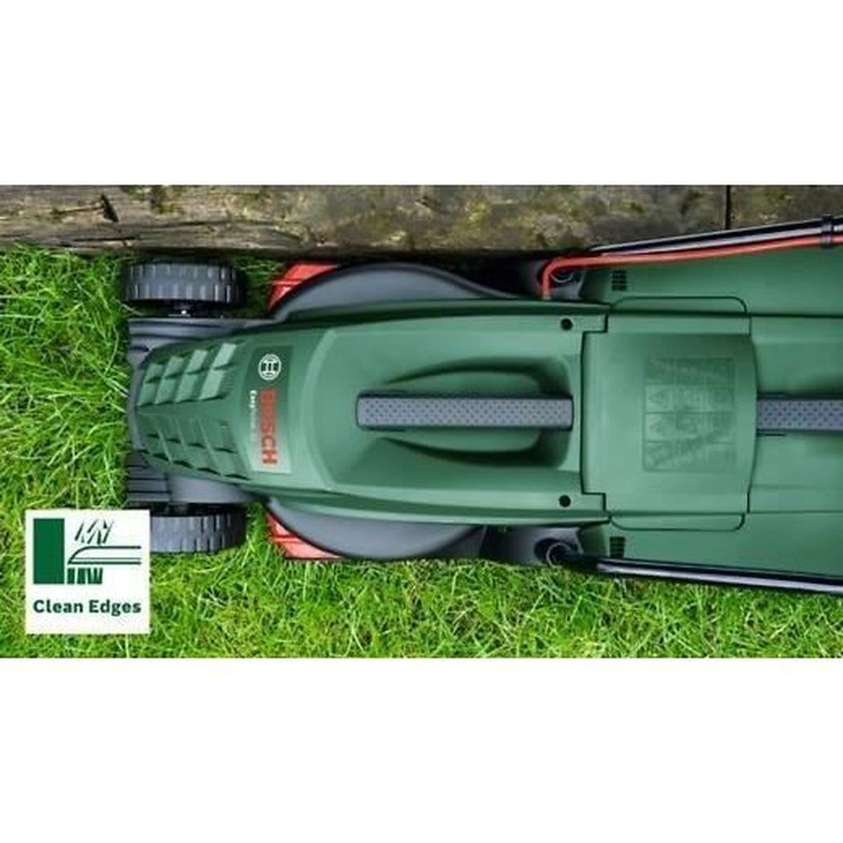 Grüner Rasenmäher mit Kabeln auf Gras neben Holz.