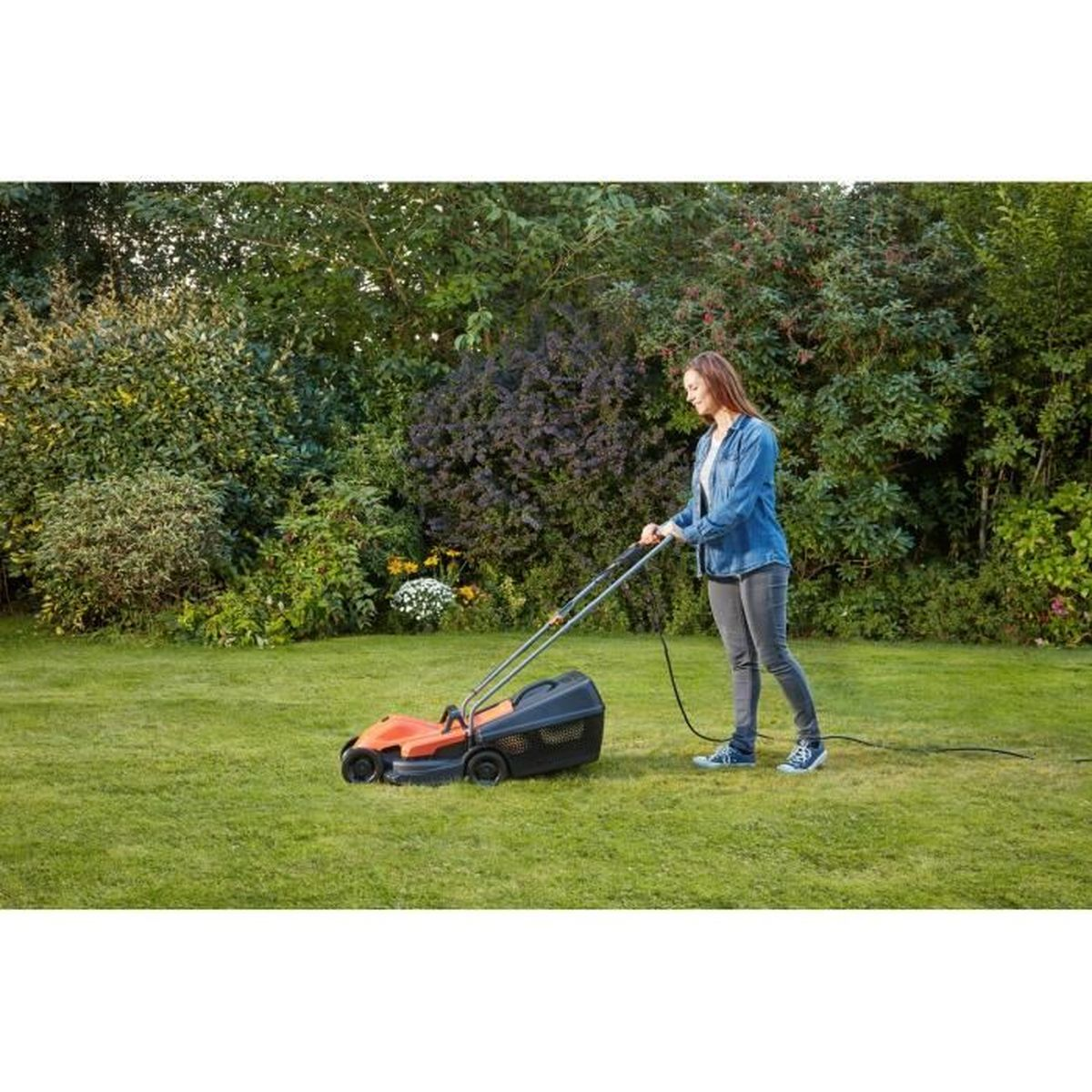 Frau mäht Rasen im Garten mit einem orange-schwarzen Elektrorasenmäher.