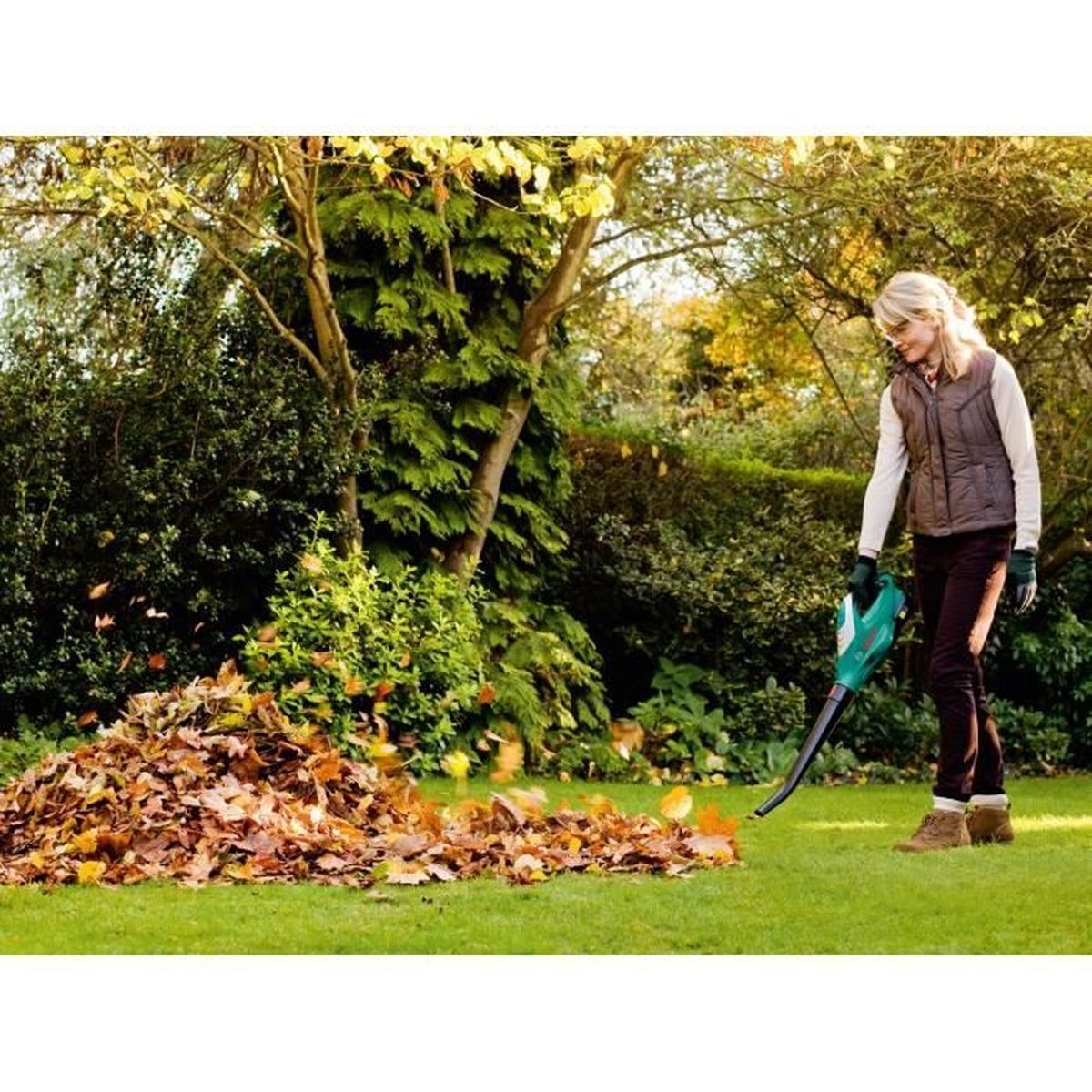 Kobieta używa dmuchawy do liści do zgarniania liści w stos w ogrodzie.