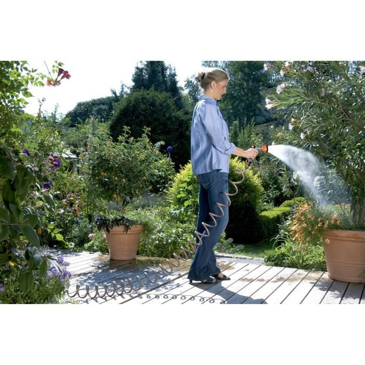Frau gießt Pflanzen im Garten mit einem Schlauch auf einer Holzterrasse.