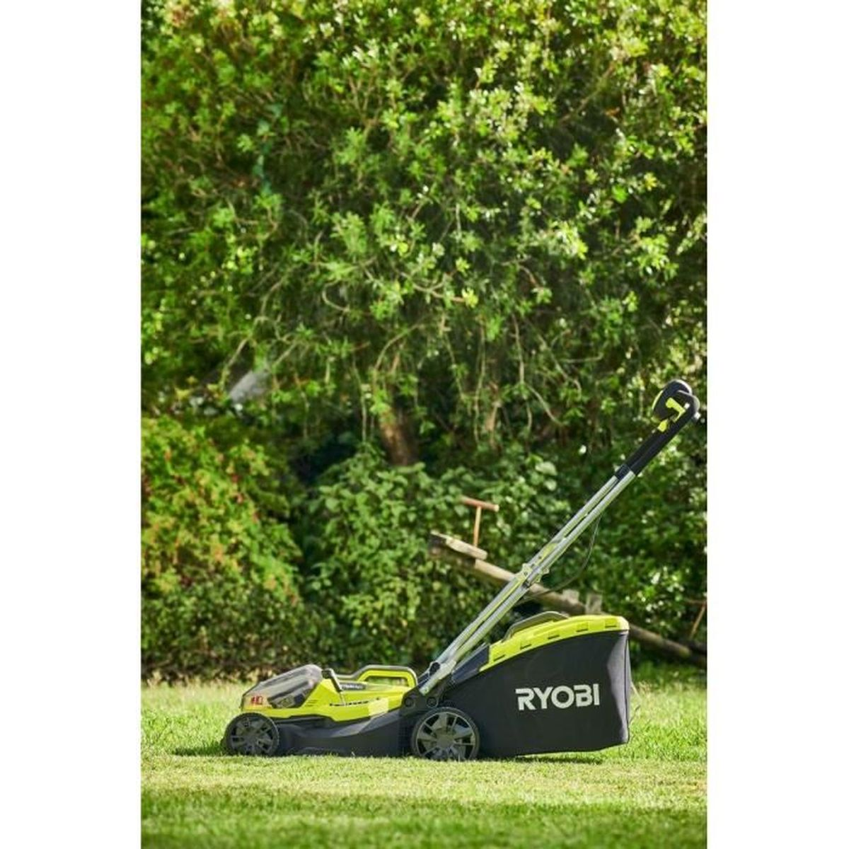 Ein grüner Ryobi Rasenmäher steht auf einem Rasen vor Bäumen.