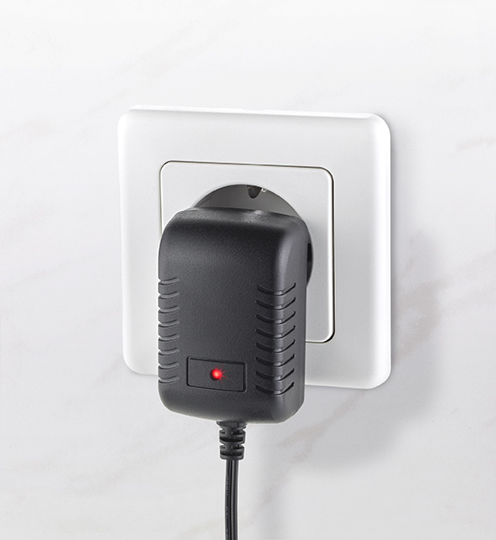 Czarny zasilacz z czerwoną diodą jest podłączony do białego gniazdka ściennego.