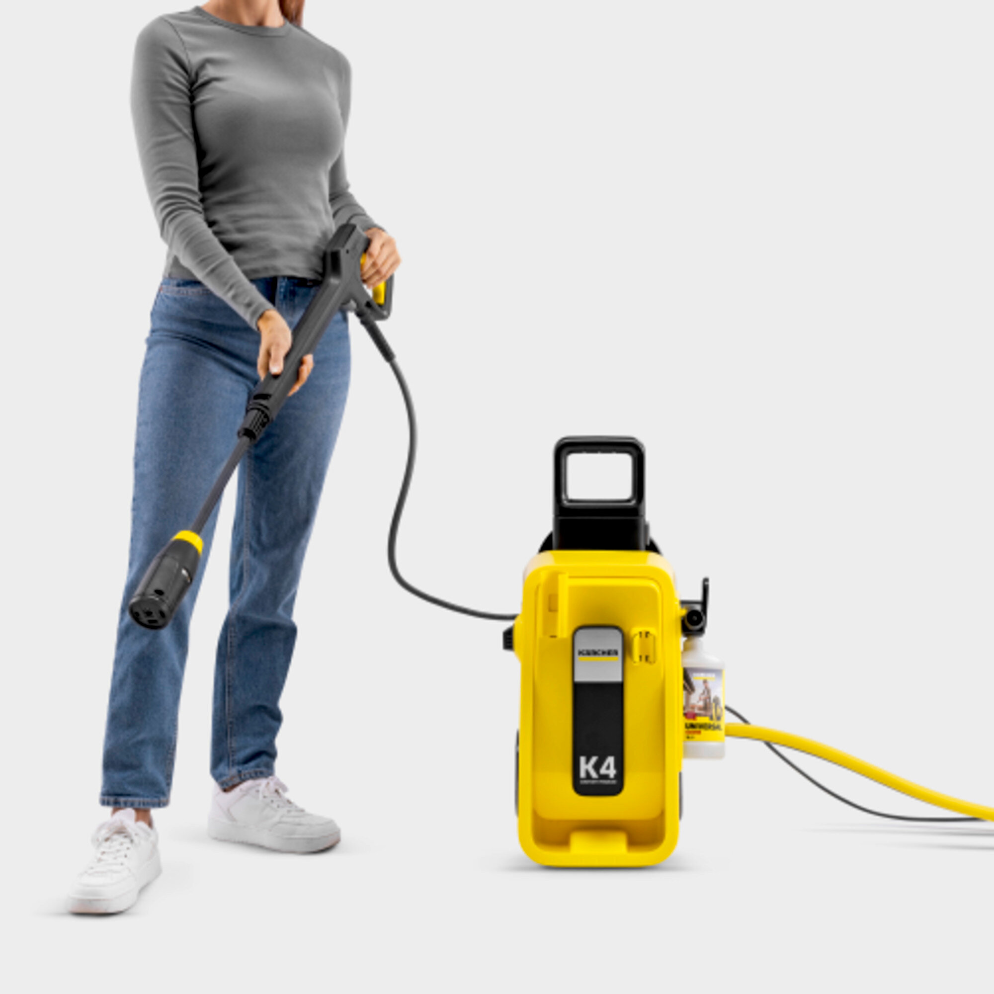 Kobieta w dżinsach trzyma uchwyt myjki ciśnieniowej obok żółtej maszyny K4.