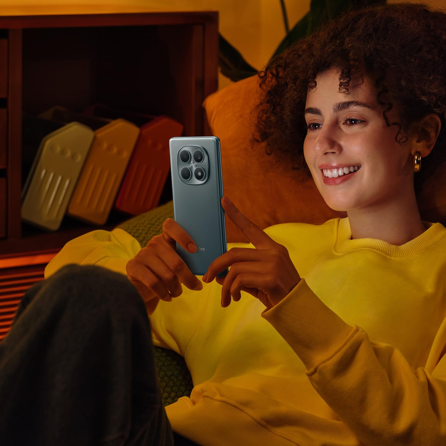 Eine Frau mit lockigem Haar lacht, während sie ein Smartphone hält.