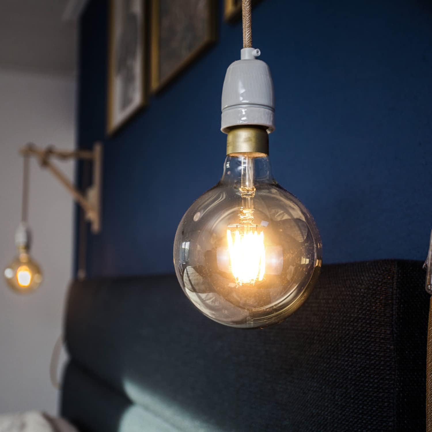 Una grande lampadina Edison rotonda pende da un cavo contro un muro blu, illuminata dall'interno.
