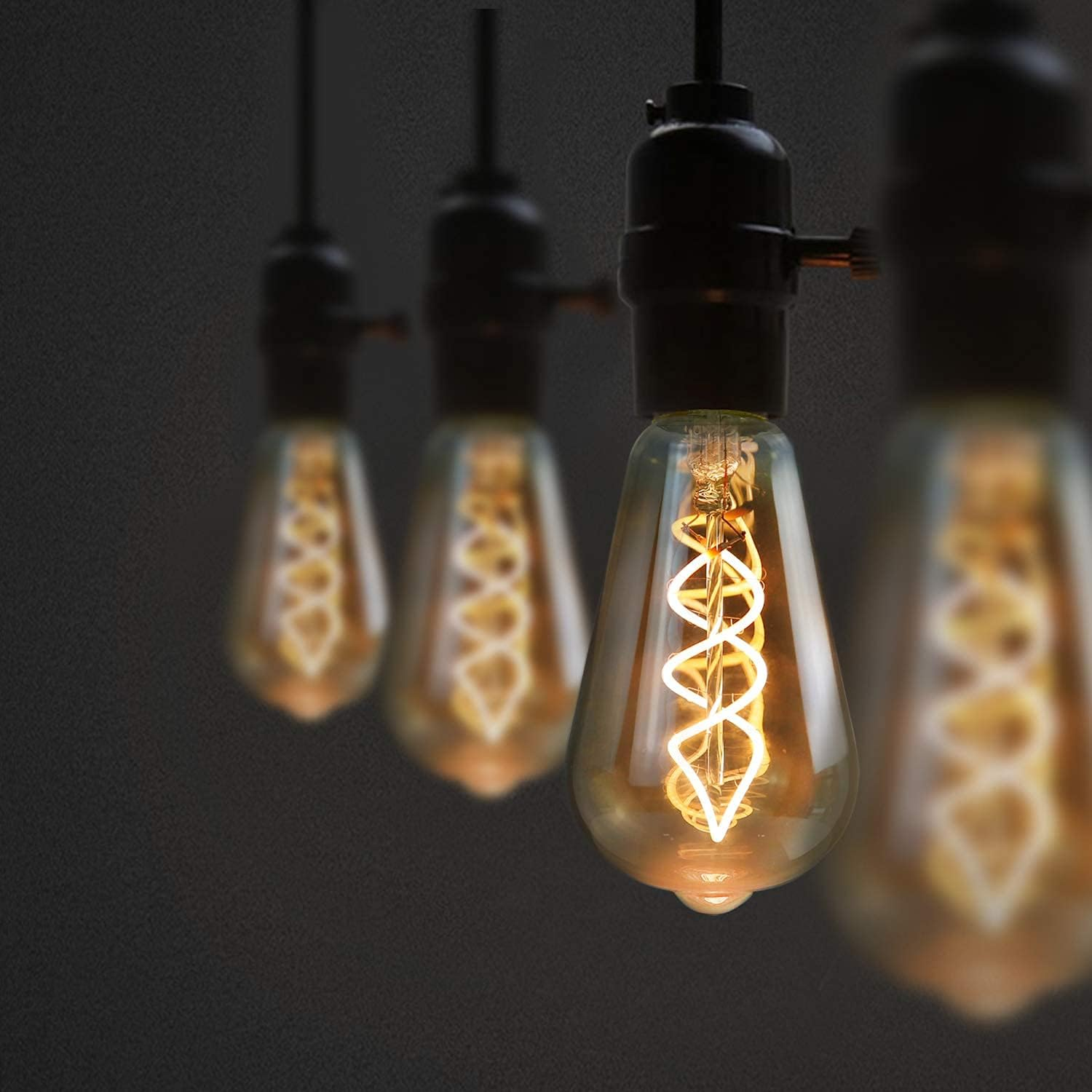Quattro lampadine Edison con filamenti a spirale visibili pendono da cavi scuri.