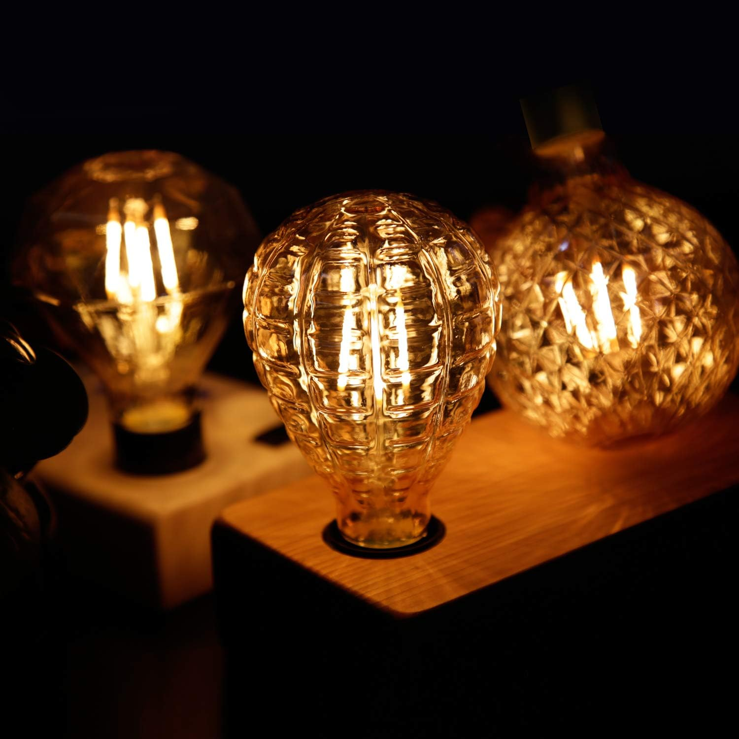 Tre lampadine decorative su basi di legno brillano caldamente al buio.