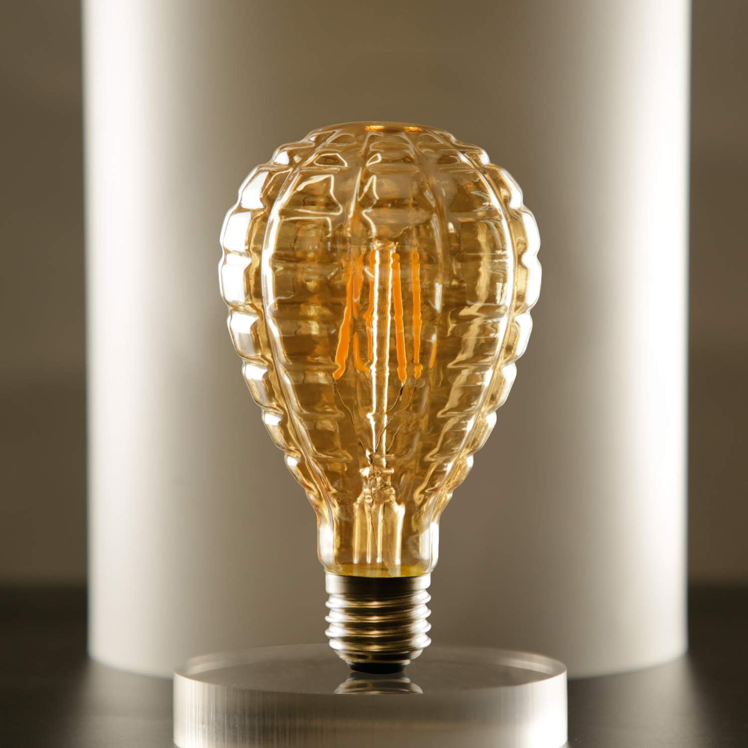 Una lampadina color ambra scanalata, simile a una pigna, si erge su un supporto.