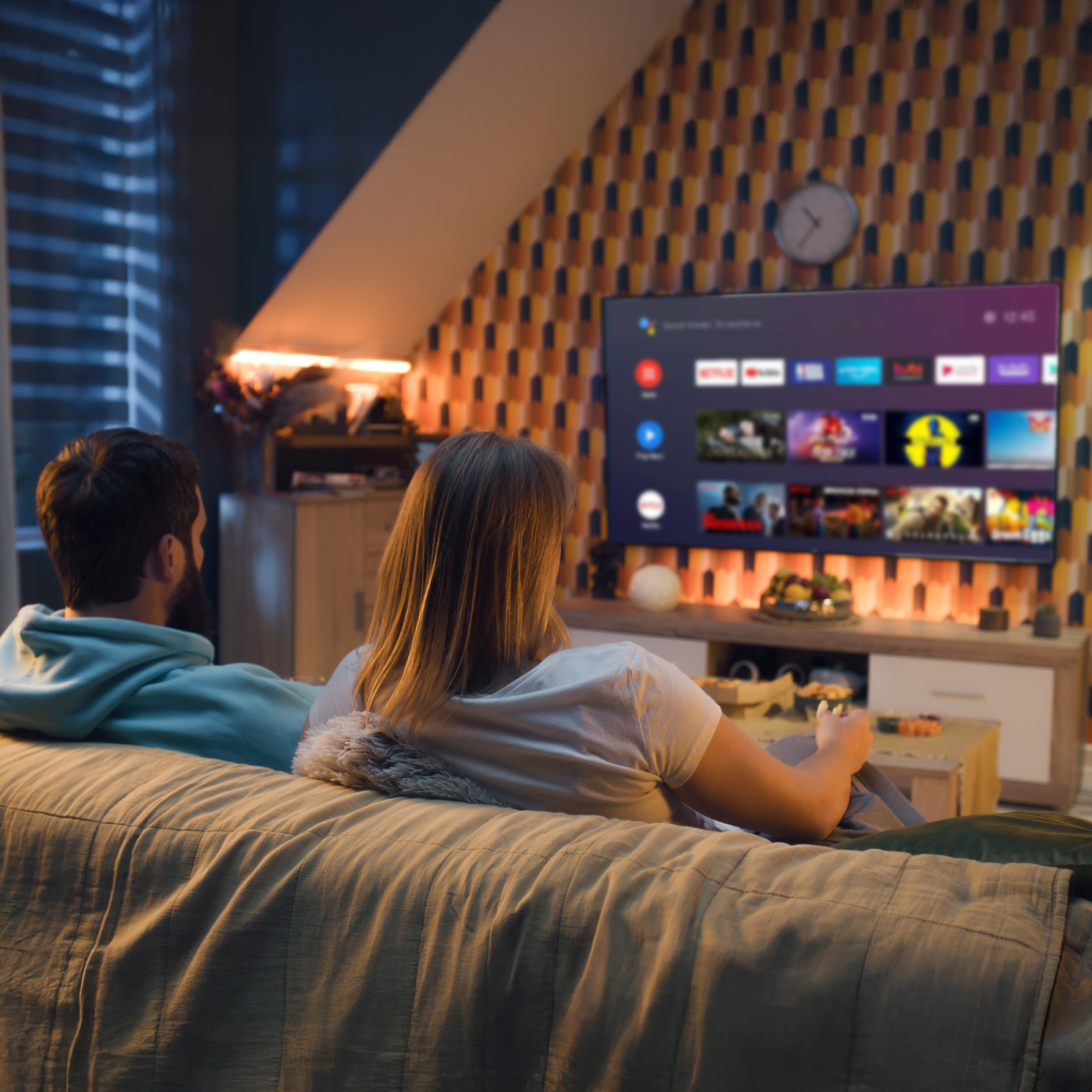Para ogląda telewizję. Ściana ma wzór. Telewizor wyświetla aplikacje.