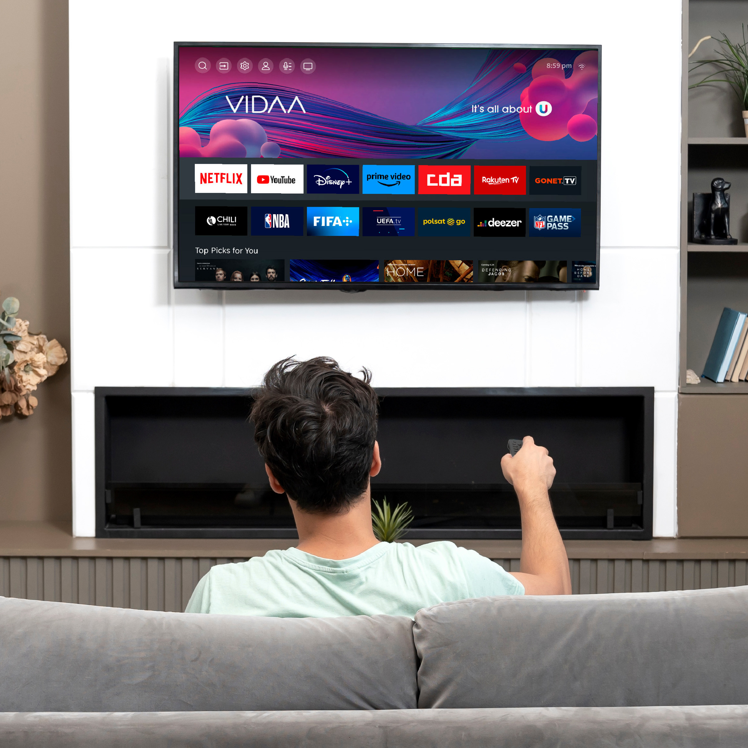 Mężczyzna siedzi na kanapie, trzyma pilot, ogląda Smart TV z aplikacjami.