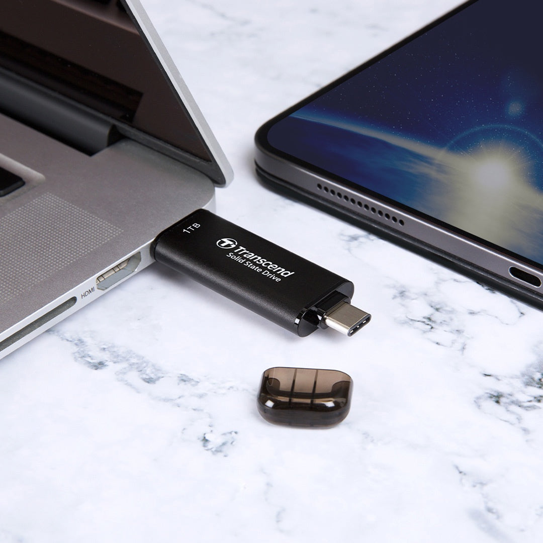 Czarny pendrive Transcend USB-C podłączony do laptopa obok tabletu.