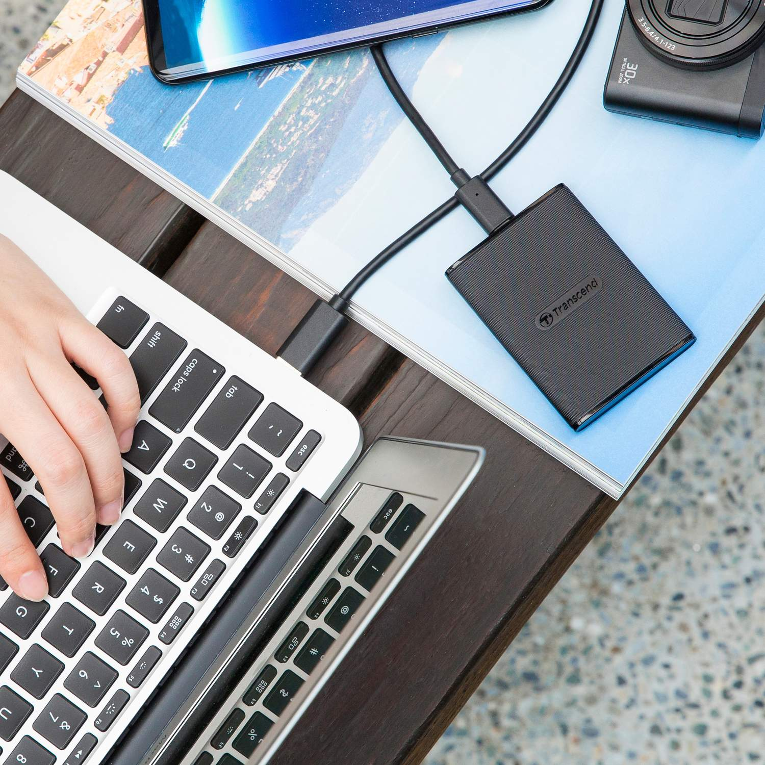 Laptop, zewnętrzny dysk twardy, smartfon i aparat na drewnianym stole.