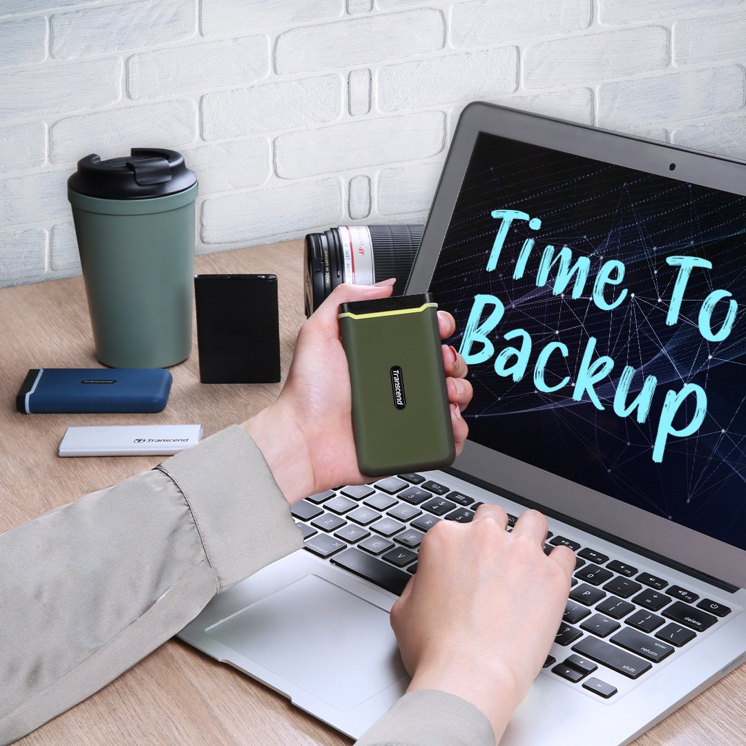 Osoba trzyma zielony dysk zewnętrzny przed laptopem z napisem "Time To Backup".