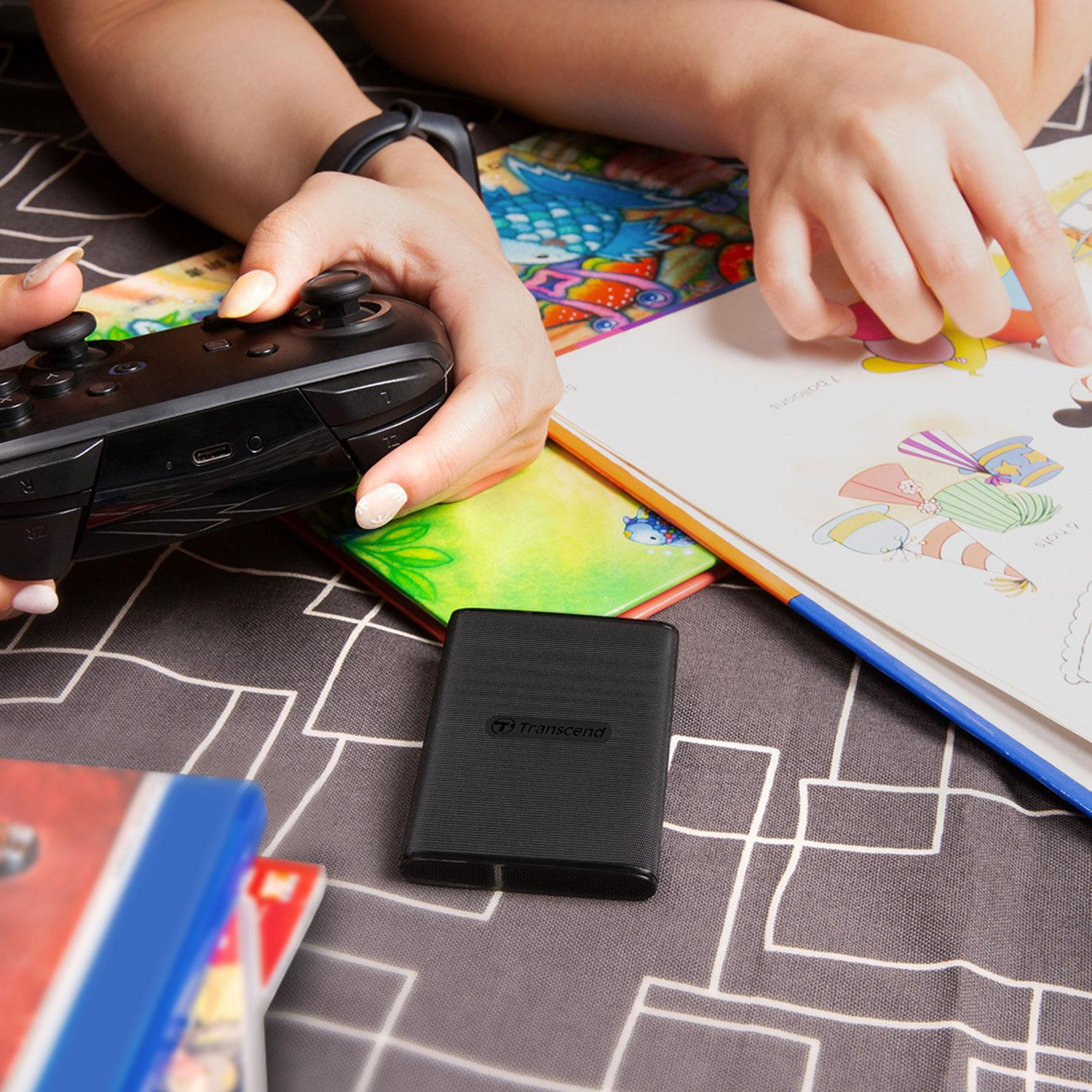 Dłonie trzymają kontroler i wskazują na książkę z kolorowymi obrazkami.