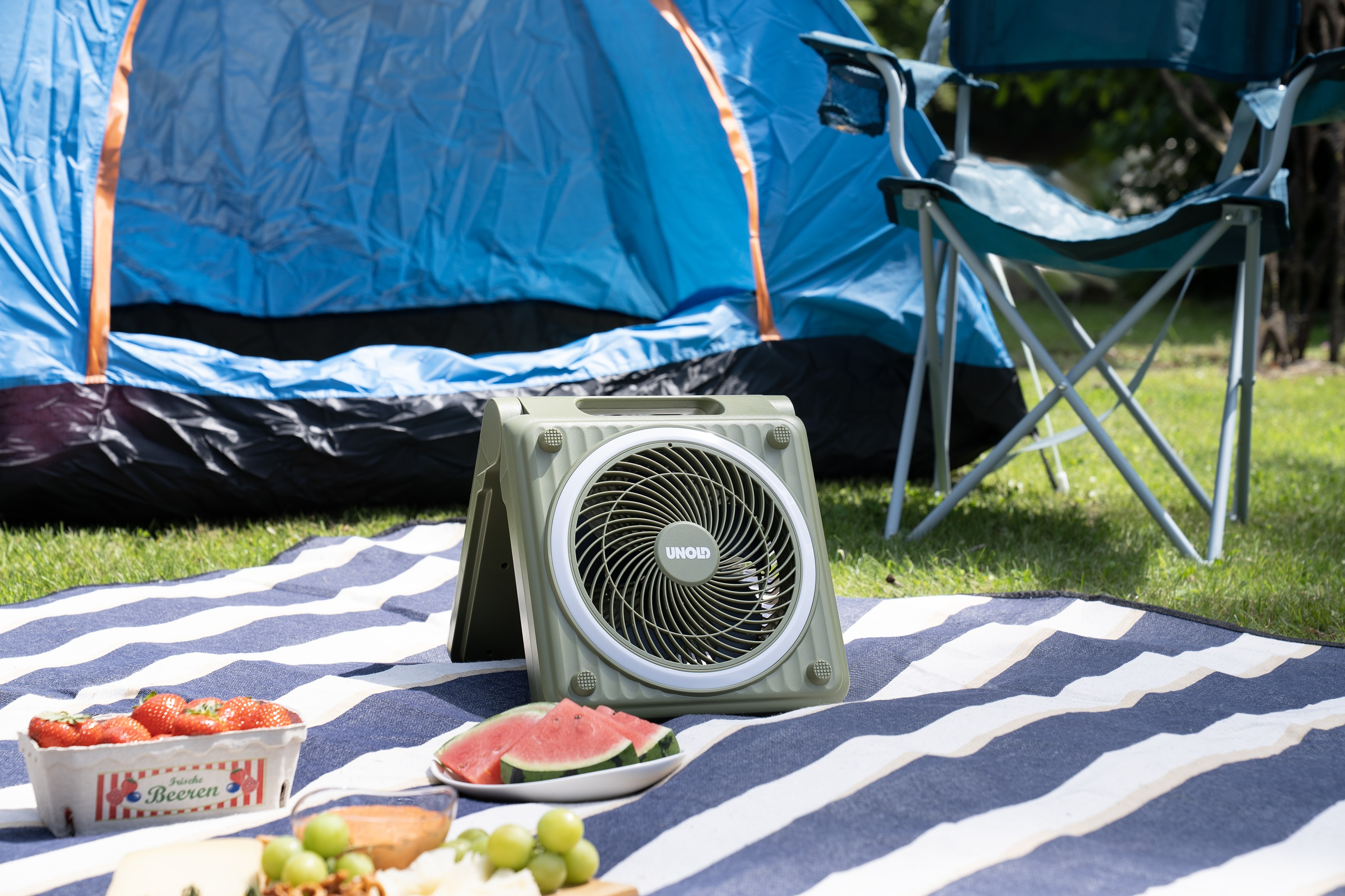Ein Campingurlaub mit Zelt, Stuhl, Ventilator und Picknick auf einer Decke.