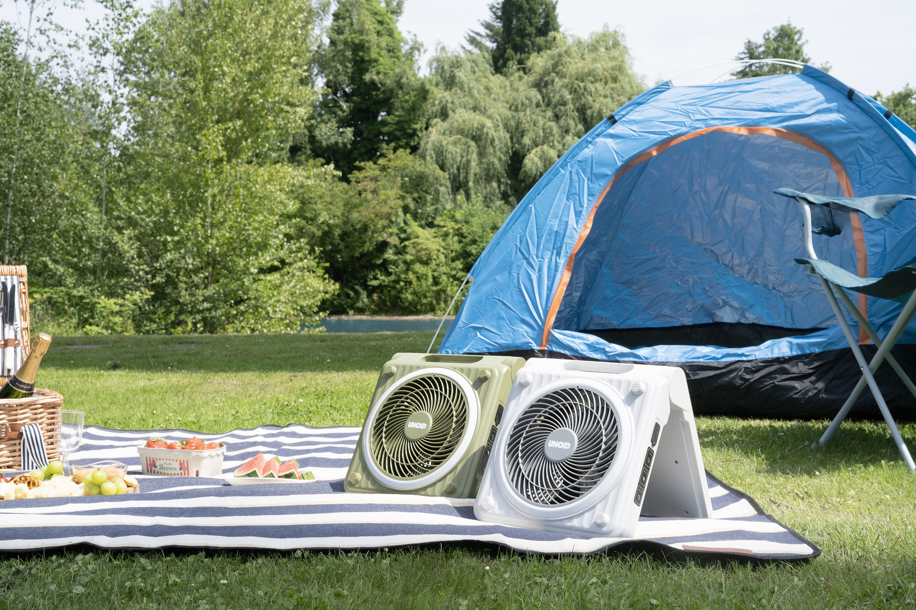 Zwei Ventilatoren vor einem Zelt mit Picknickdecke, Essen und Getränken.