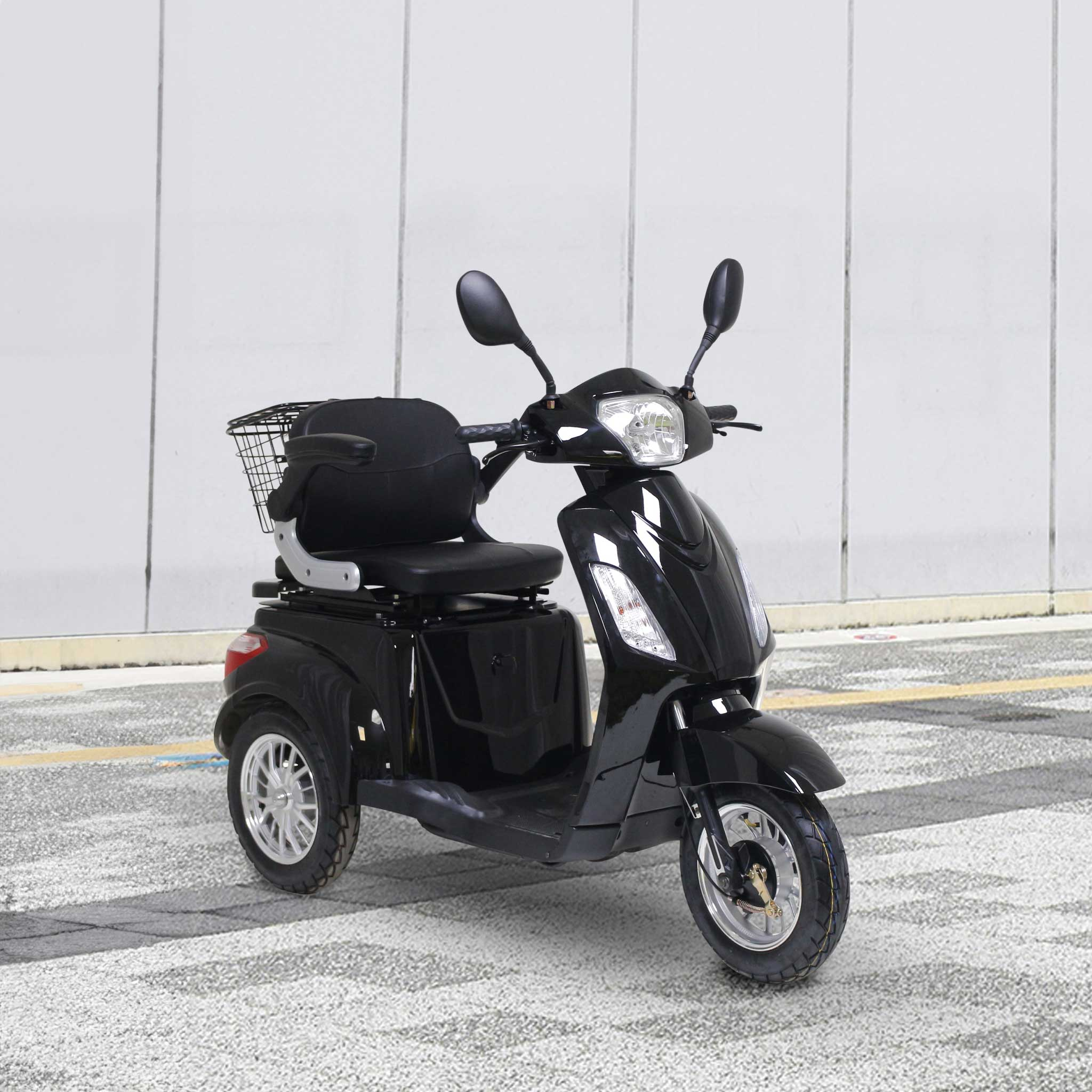 Czarny trójkołowy skuter z koszem stoi na asfalcie przed ścianą.