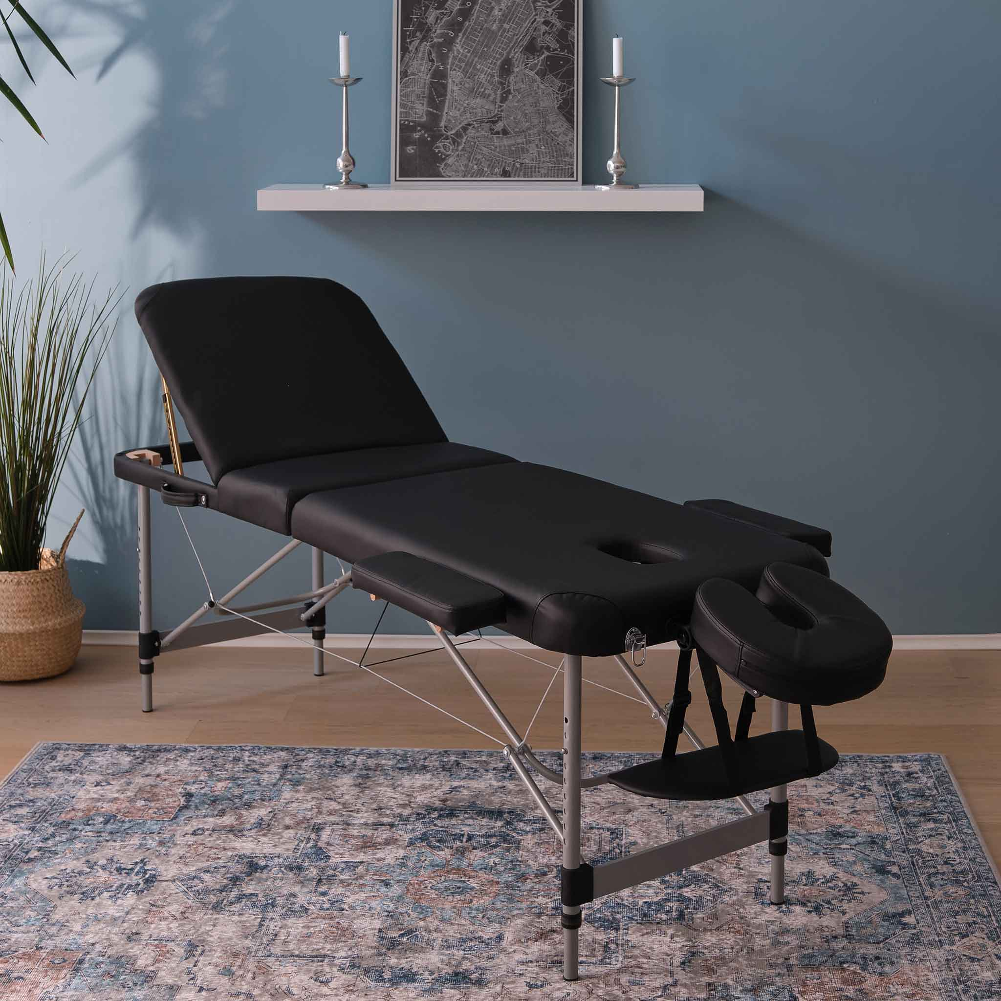 Schwarzer Massagetisch mit Kopfstütze auf einem Teppich vor blauer Wand.