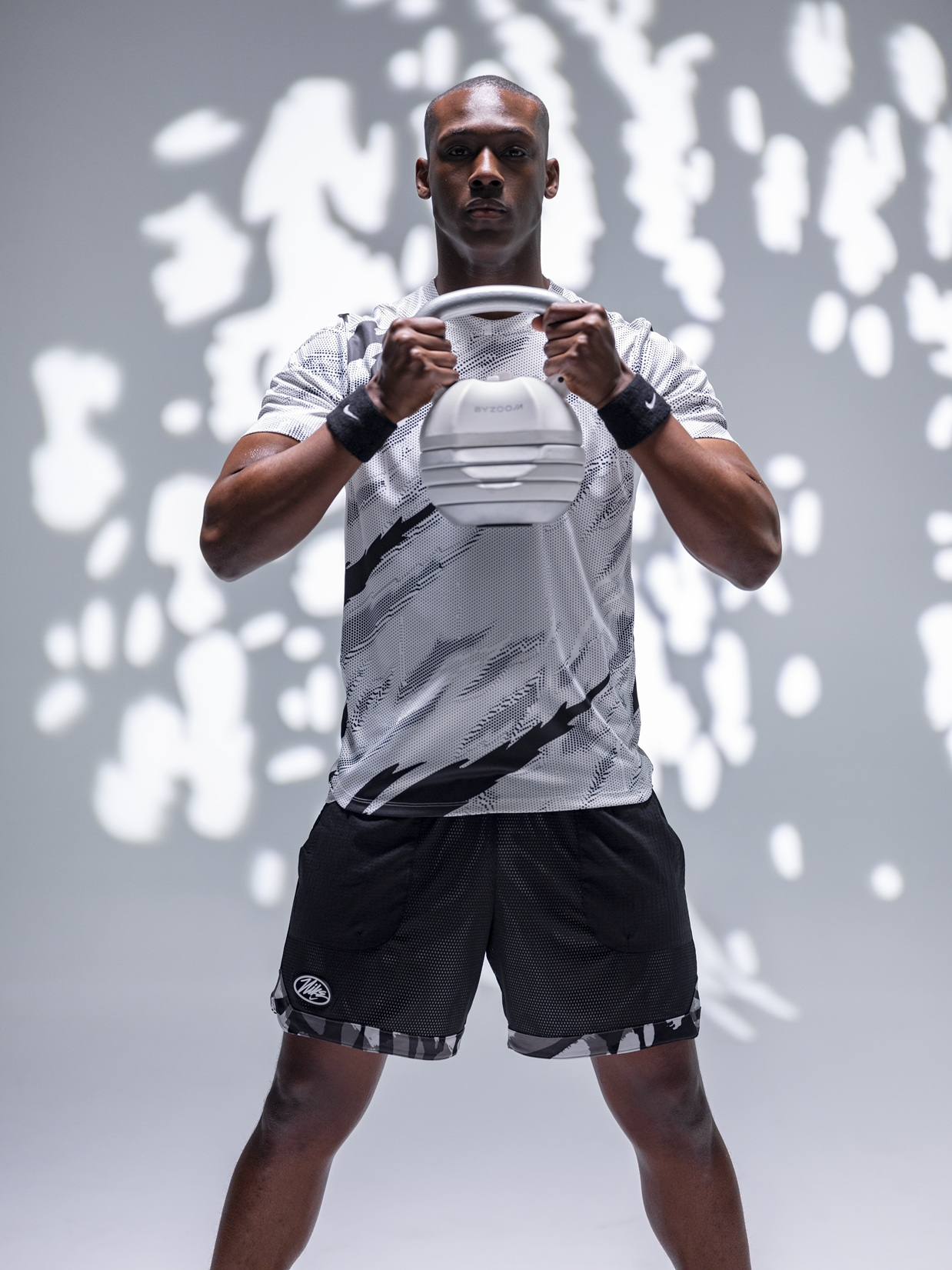 Ein Mann hält ein weißes Kettlebell mit schwarzem Muster-Shirt und Shorts.