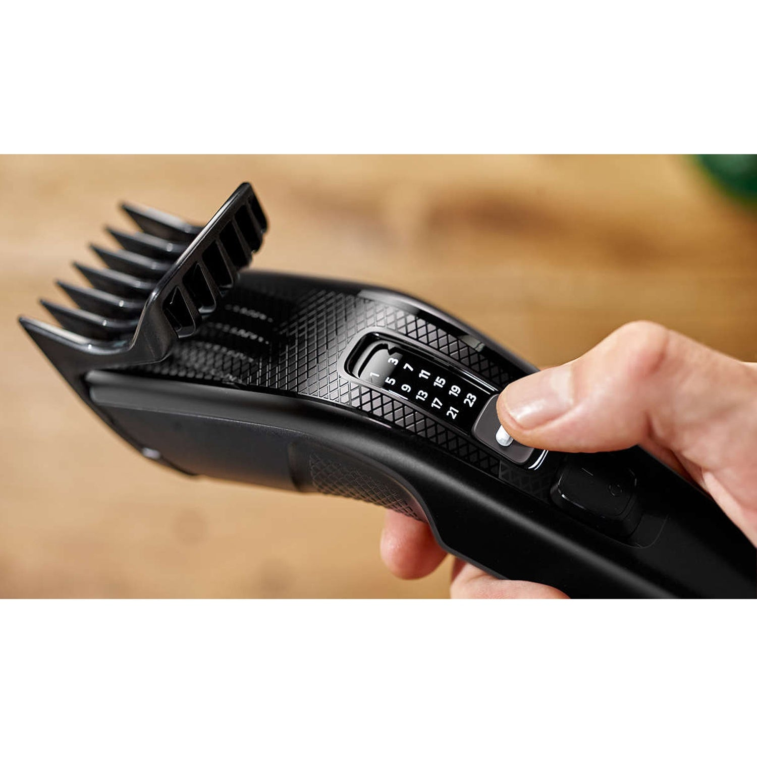 Eine Hand passt die Längeneinstellung eines schwarzen Haarschneiders an.