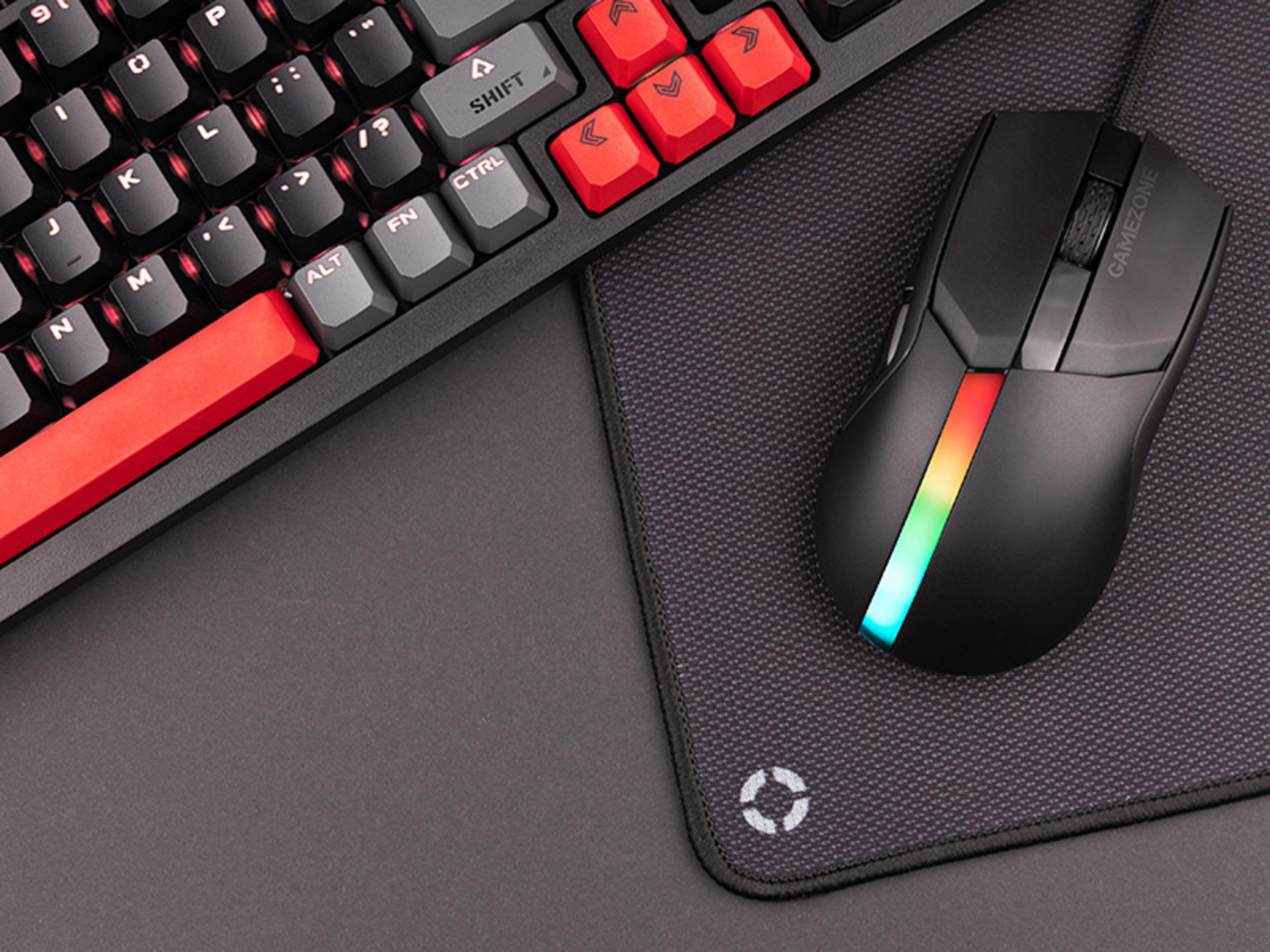 Souris gaming noire avec éclairage RVB sur un tapis de souris à côté d'un clavier.