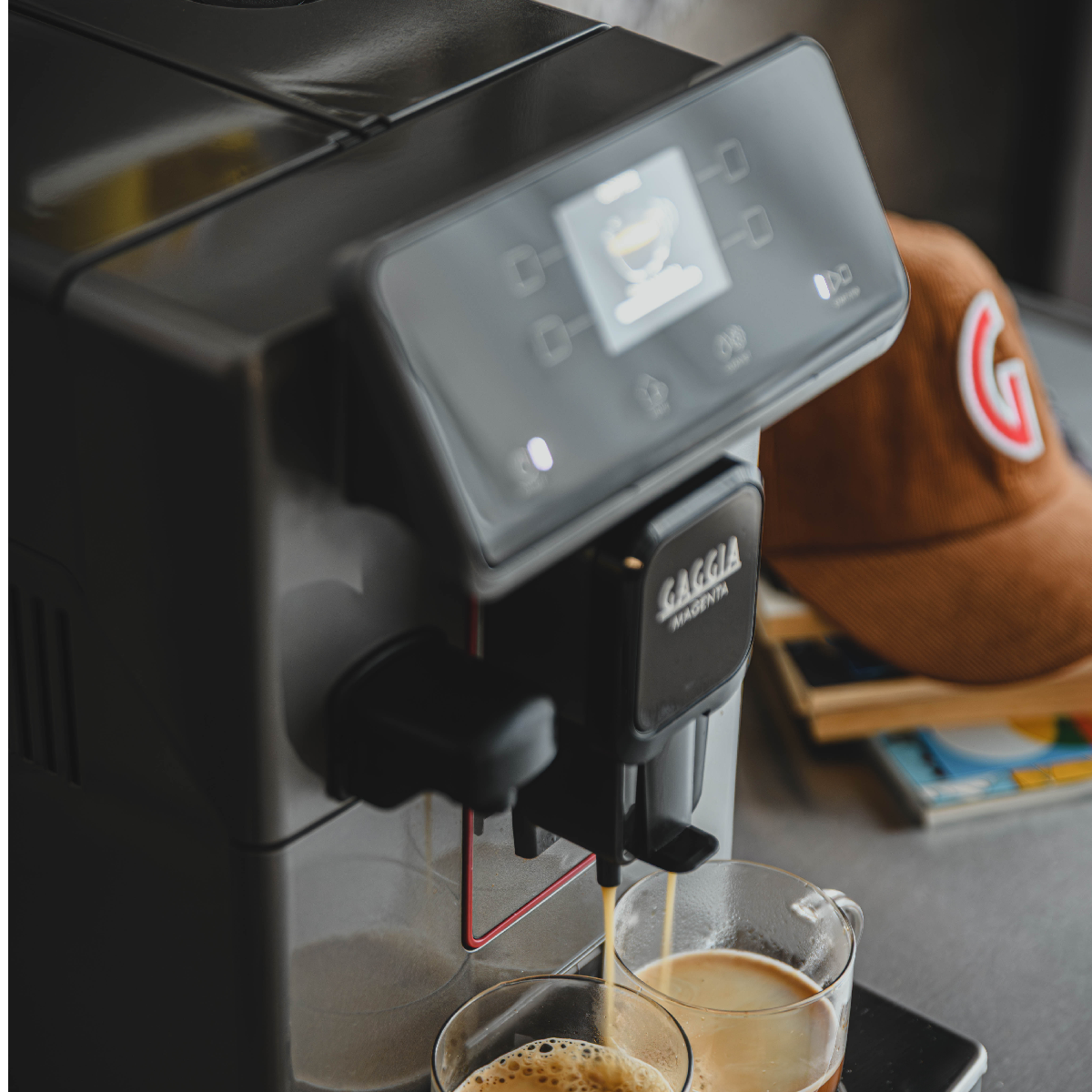 Kaffeemaschine brüht Kaffee in zwei Tassen; braune Kappe im Hintergrund.