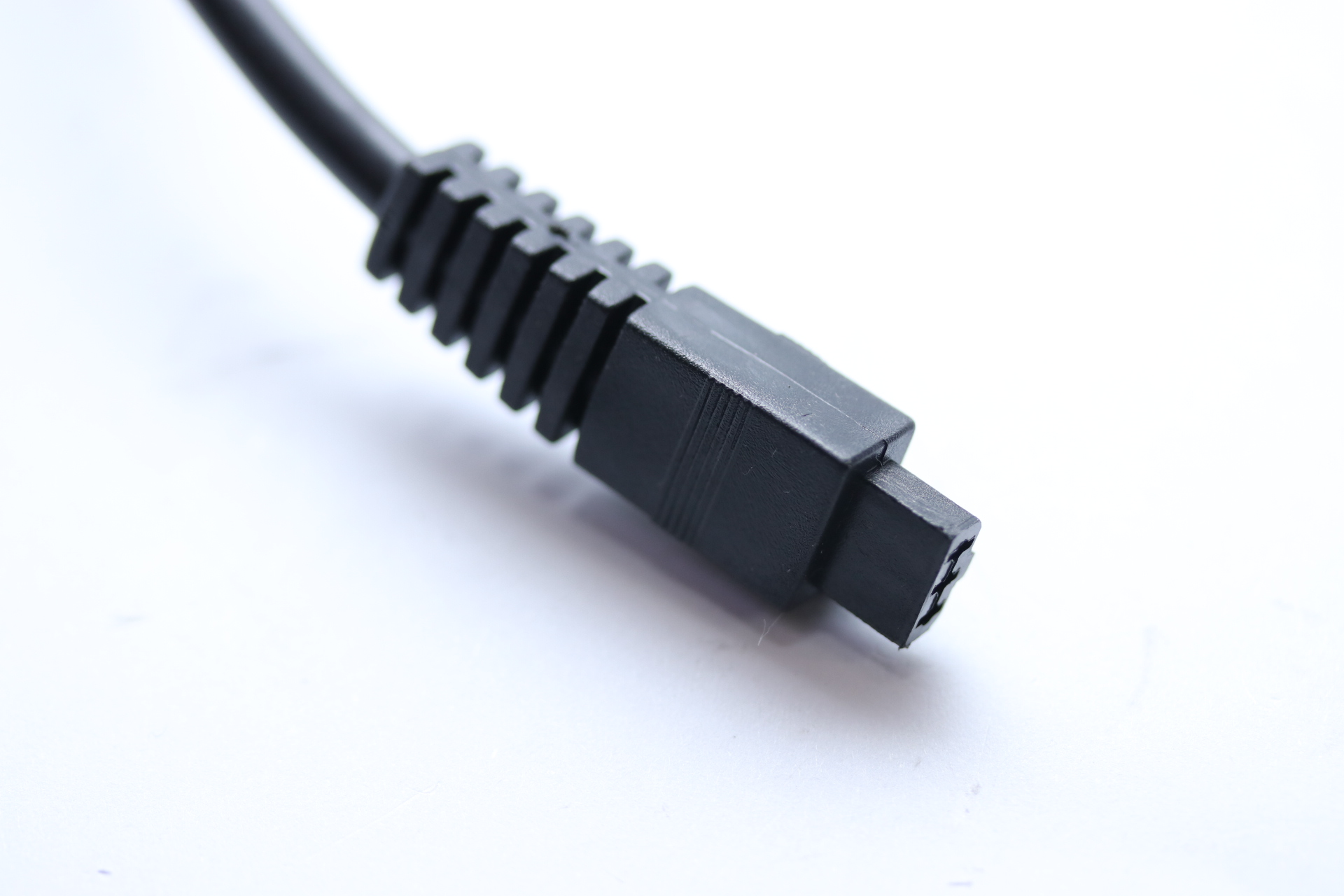 Schwarzer Stecker mit Rillen und drei Pins auf weißem Hintergrund.