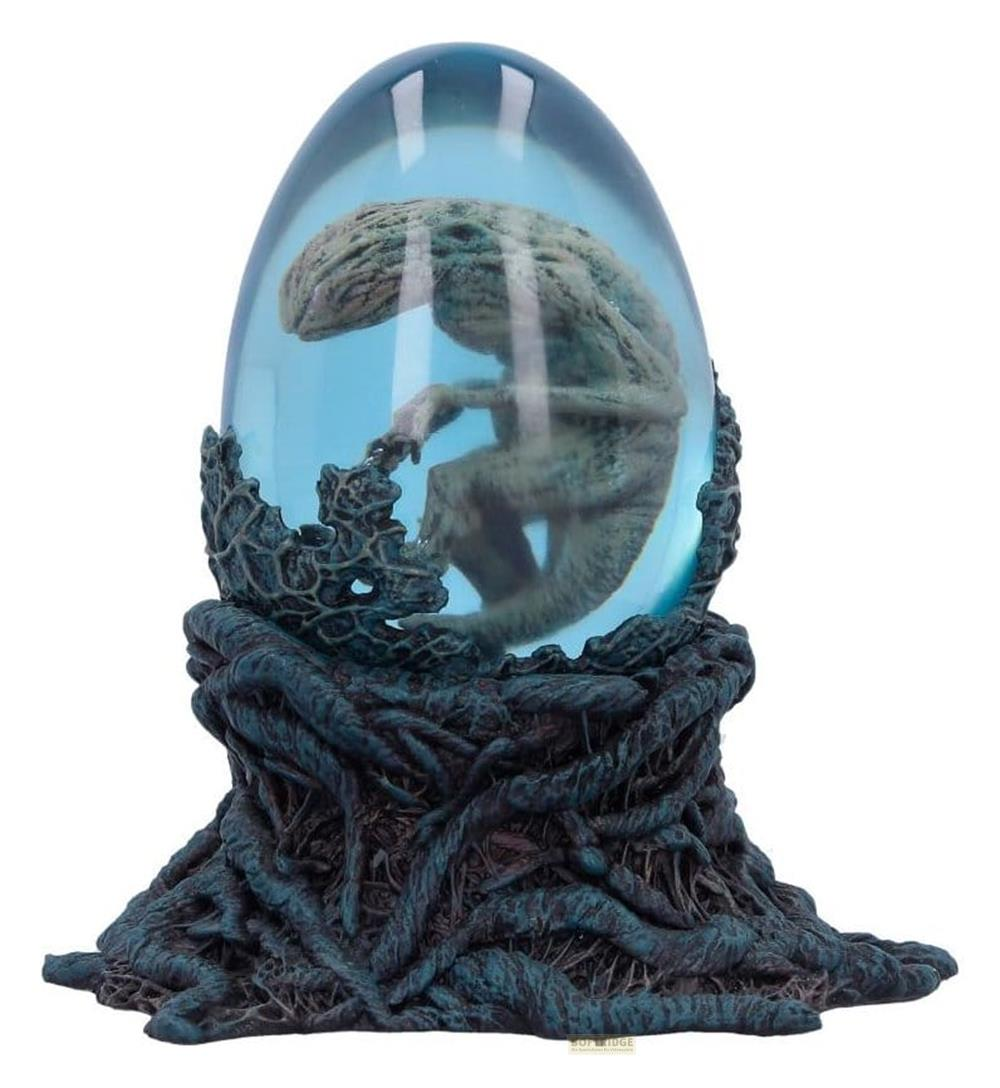 Ein grünes Alien-Baby in einem blauen Ei auf einem dunklen Sockel.