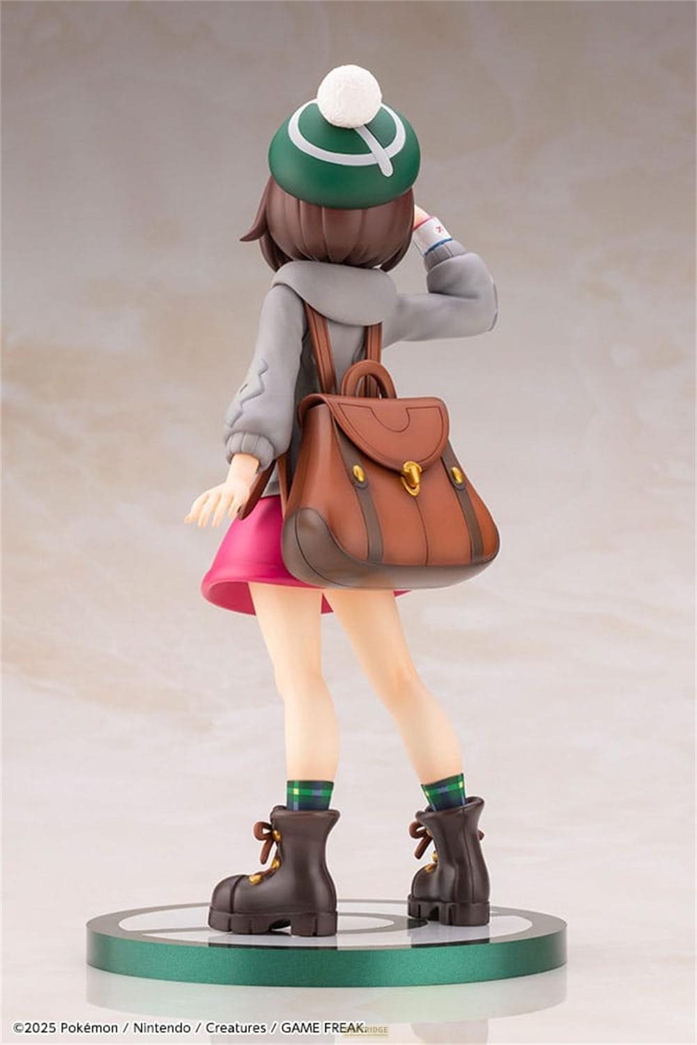 Statua di una ragazza con cappello verde, giacca grigia e gonna rosa.