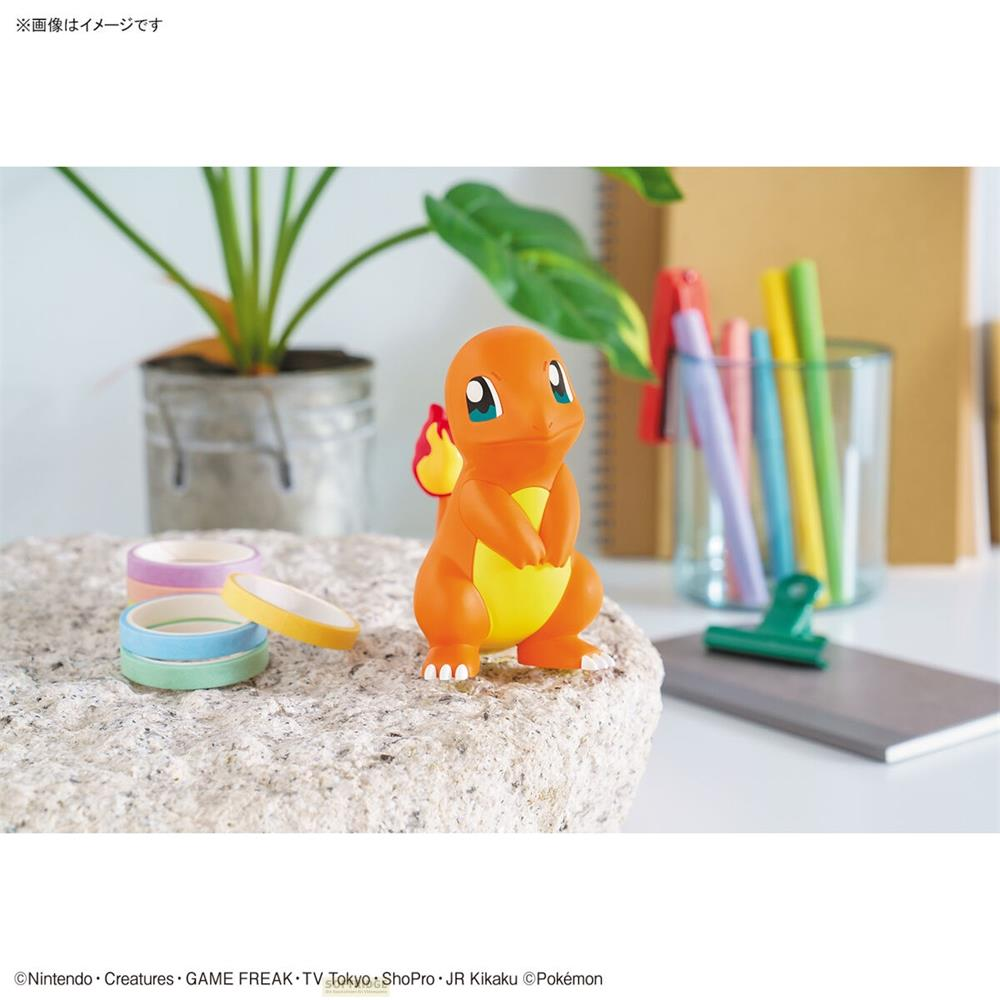 Ein orangefarbener Charmander-Charakter sitzt auf einem Stein neben Klebebandrollen.