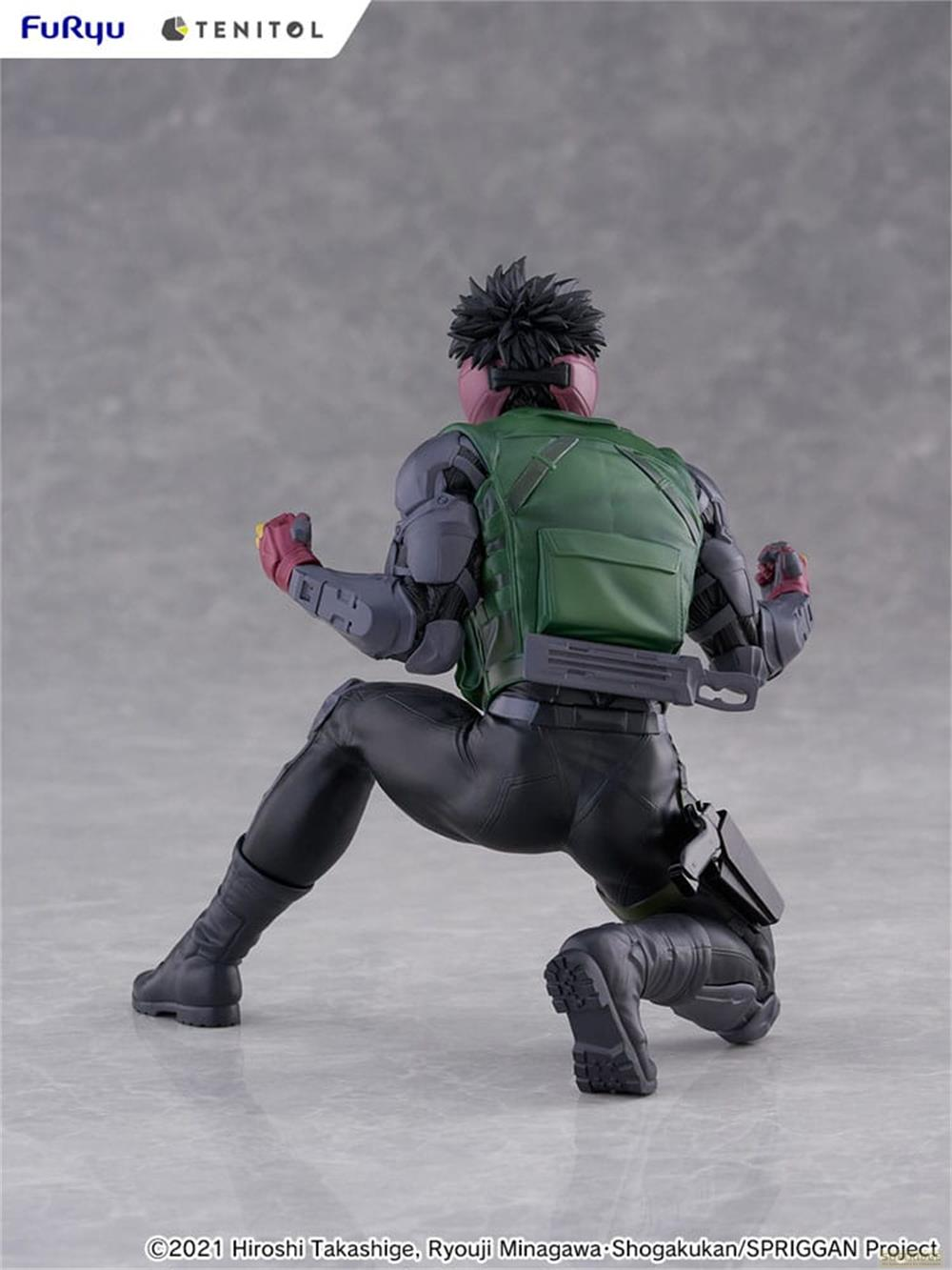 Eine Actionfigur in grüner Weste und schwarzer Hose kniet auf grauem Untergrund.