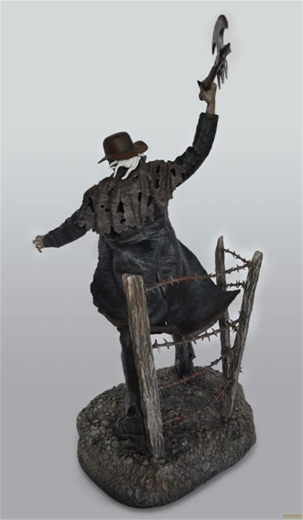 Eine Figur mit Hut und zerlumptem Umhang steht auf einem steinigen Sockel mit Stacheldraht.