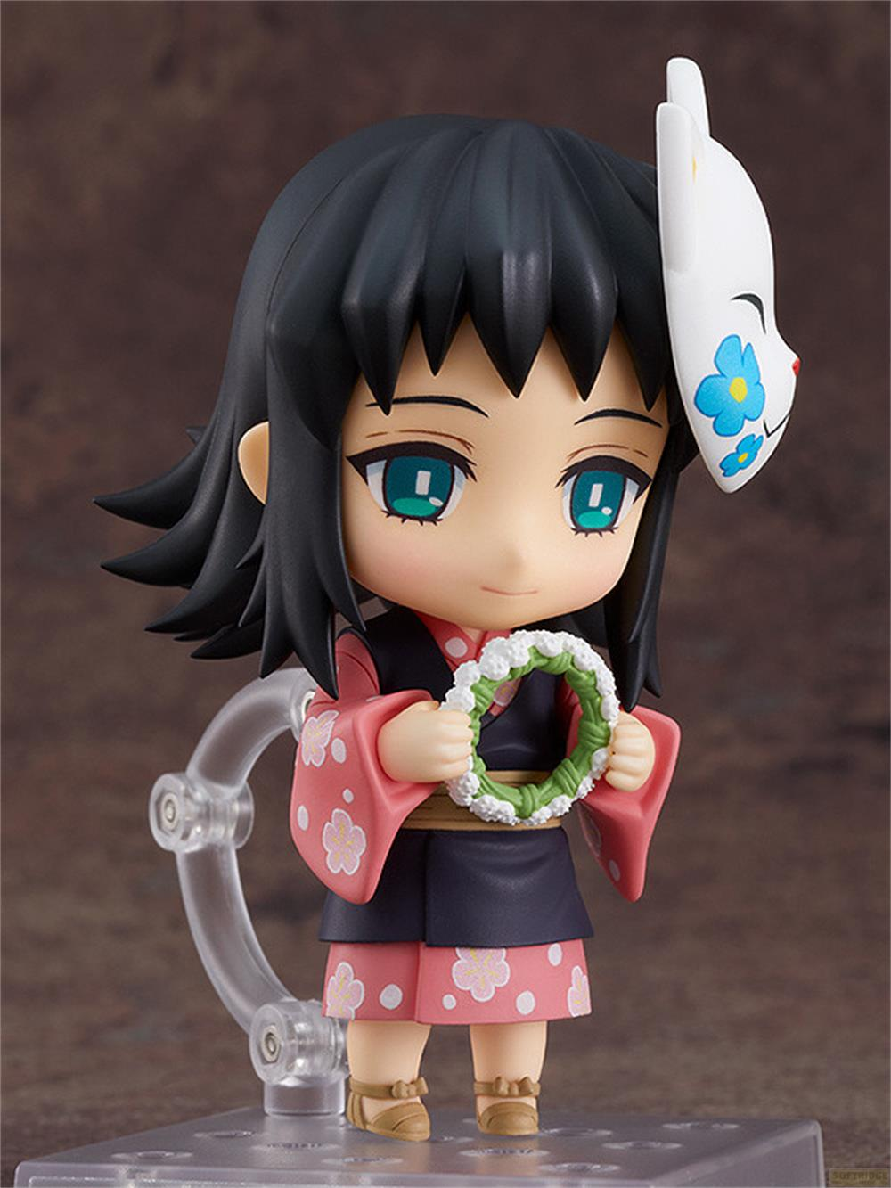 Personaggio in stile anime con capelli neri, maschera bianca e kimono rosa che tiene una ghirlanda verde.