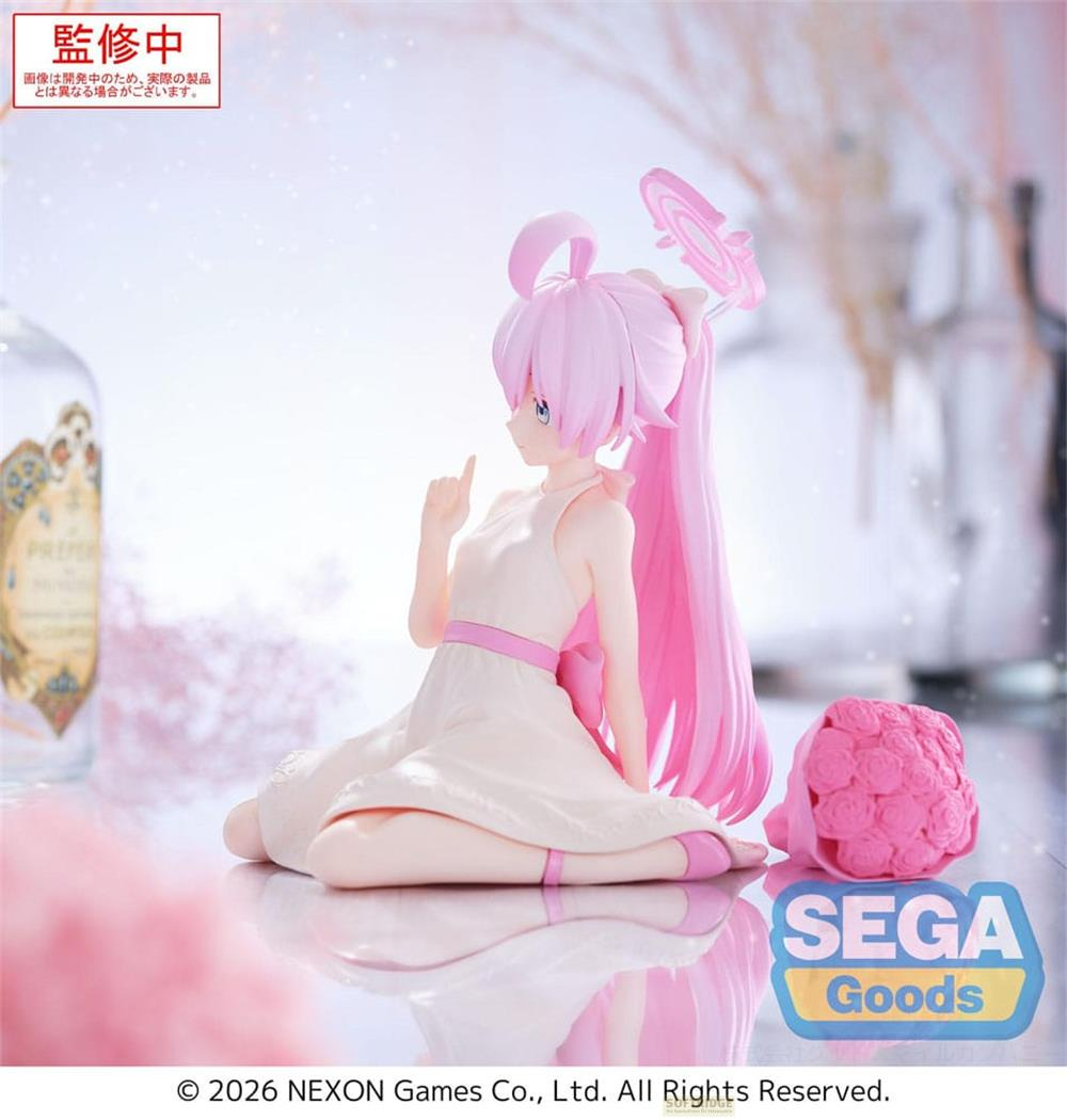 Eine pinkhaarige Figur in einem weißen Kleid sitzt auf dem Boden, neben einem Blumenstrauß.