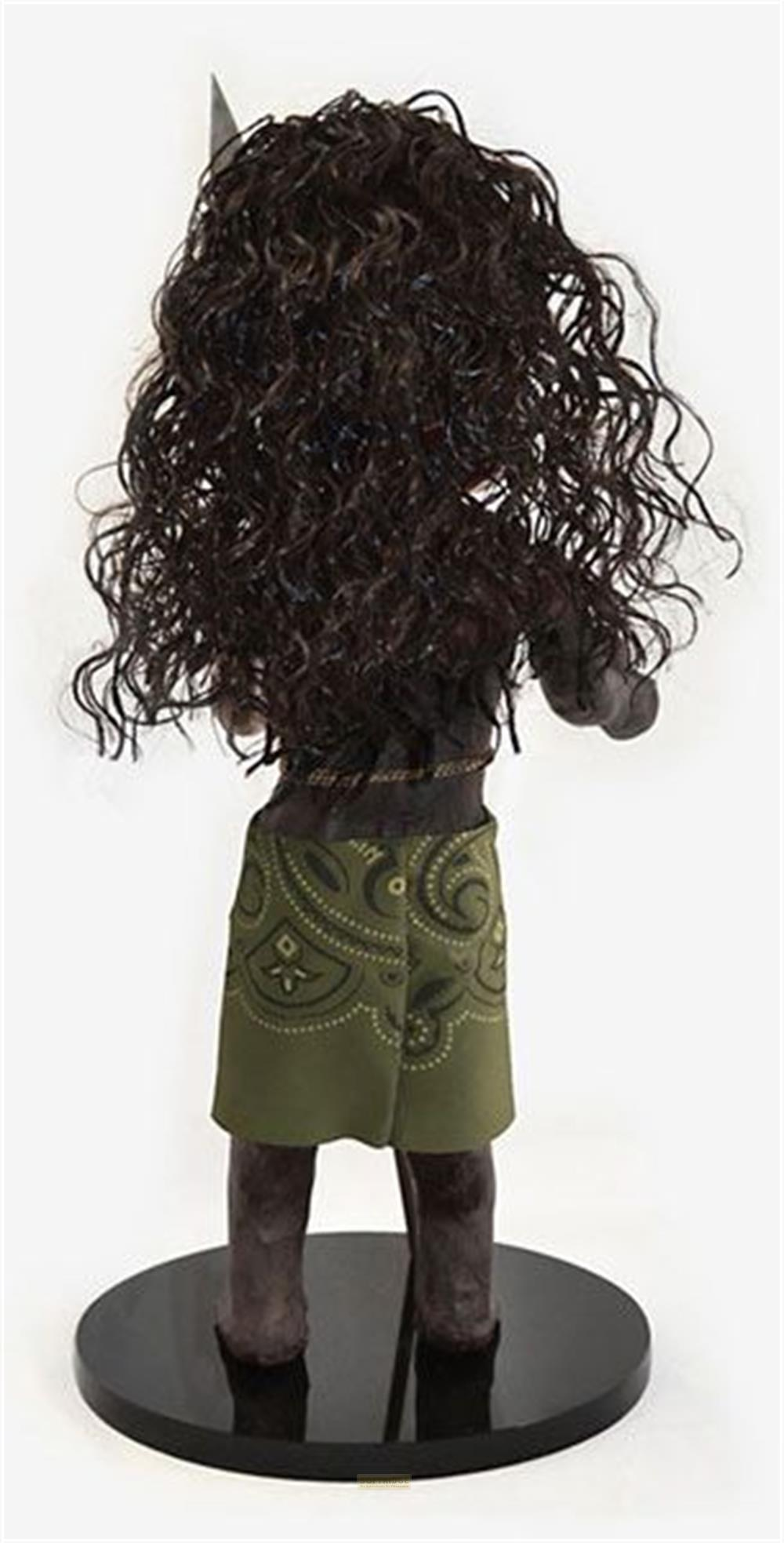 Eine Puppe mit dunklem, lockigem Haar und einem grünen Musterrock auf einem schwarzen Podest.