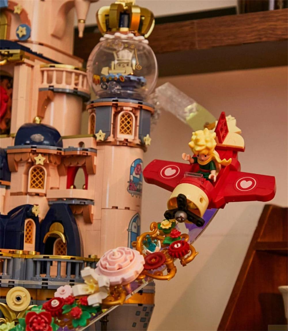 Ein Spielzeugflugzeug mit dem kleinen Prinzen fliegt vor einer rosafarbenen Burg.