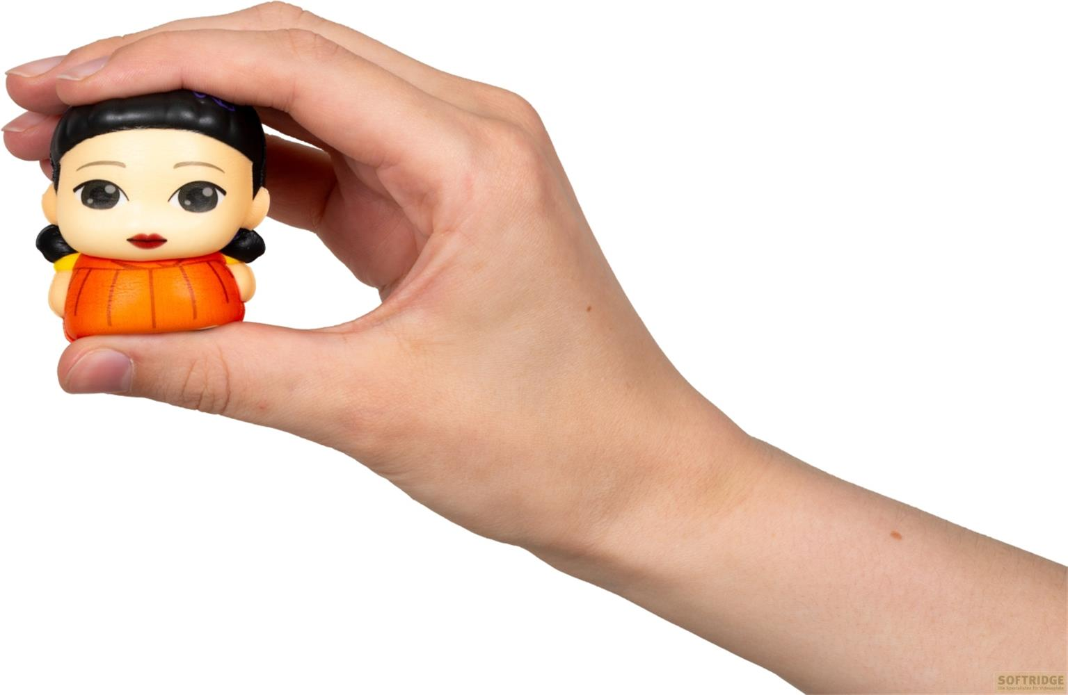 Eine Hand hält eine kleine Figur mit orangefarbenem Kleid und schwarzen Haaren.
