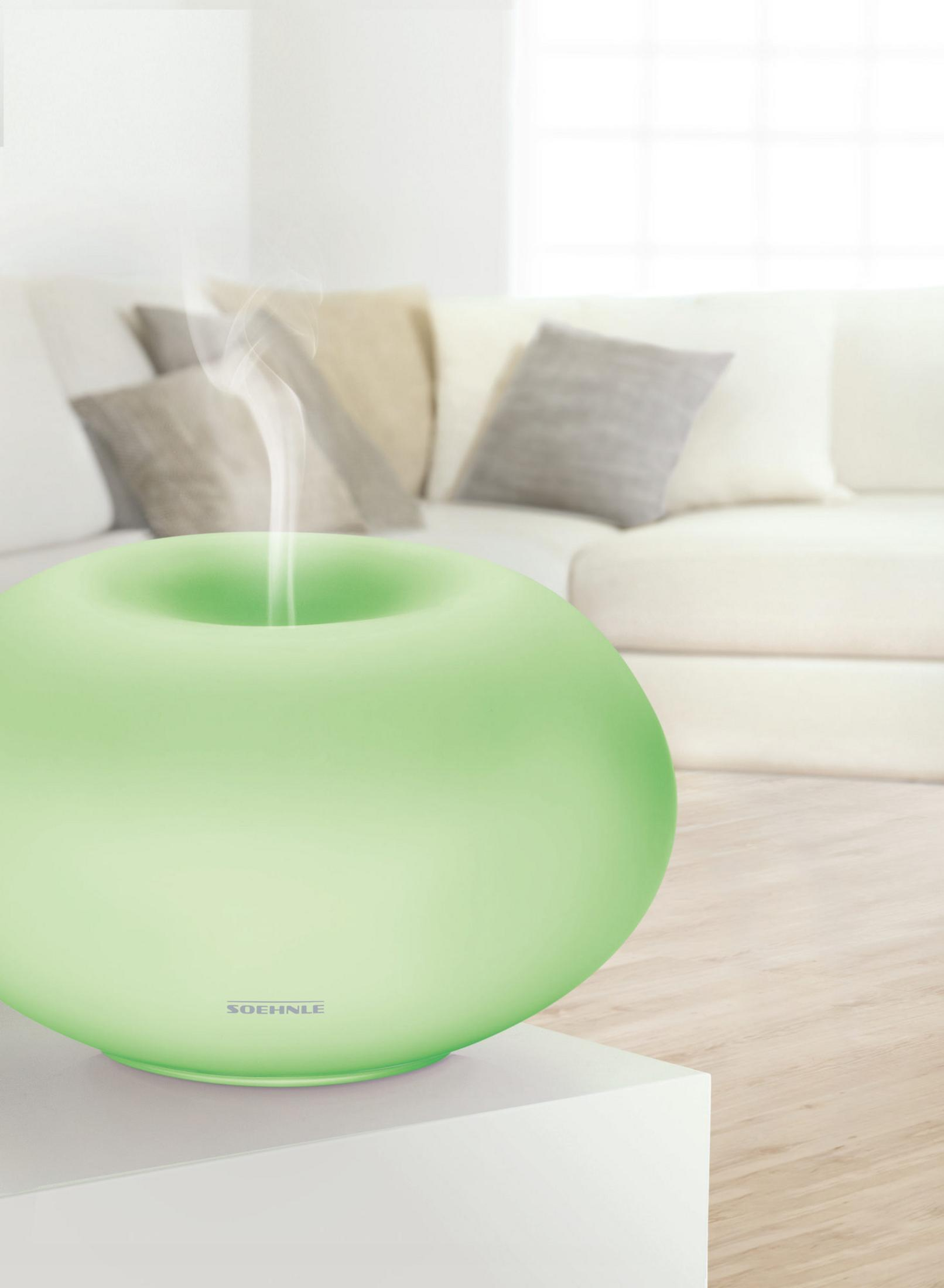 Ein grüner Aroma-Diffusor gibt Dampf in einem Wohnzimmer mit Sofa ab.