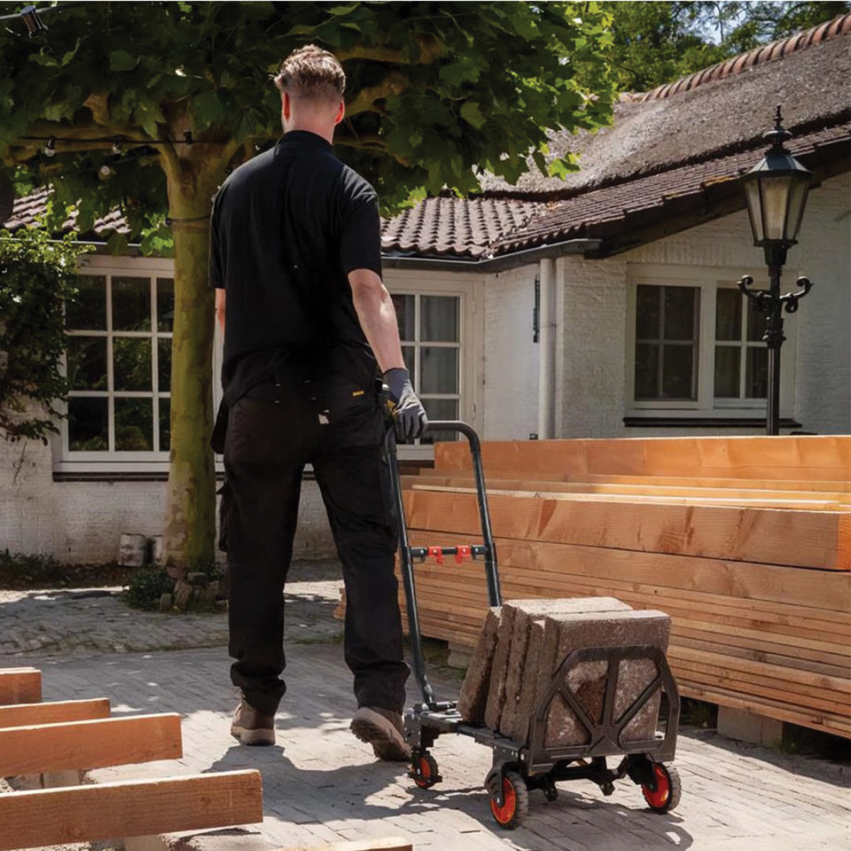 Man pushing cart with stones in front of a house with thatched roof.