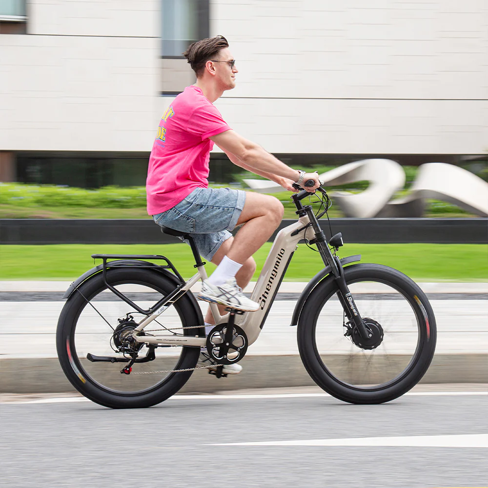 Un uomo guida una e-bike beige su un marciapiede, indossa una maglietta rosa e pantaloncini di jeans.