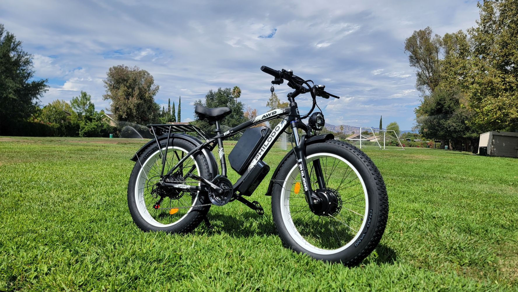 Bicicleta eléctrica negra de llantas anchas sobre césped verde, cielo azul con nubes.