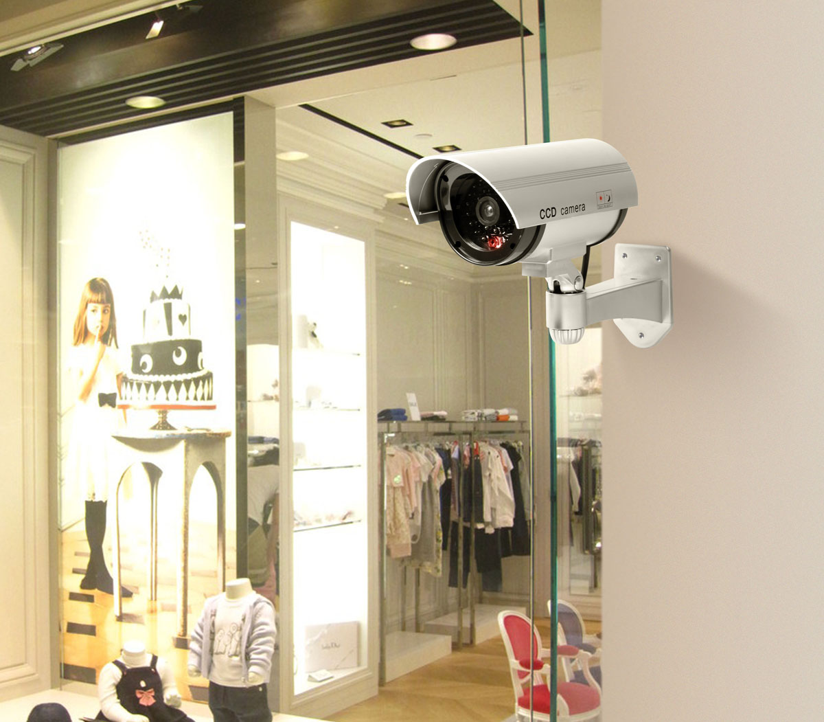 Kamera bezpieczeństwa zamontowana na ścianie przed sklepem z ubraniami i ilustracją dziewczynki.