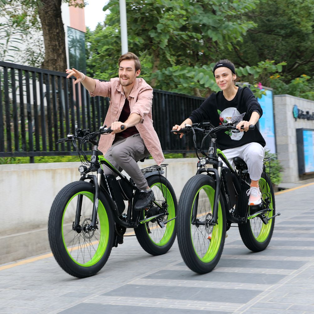 Dos personas en bicicletas eléctricas con llantas verdes circulan por un camino pavimentado.