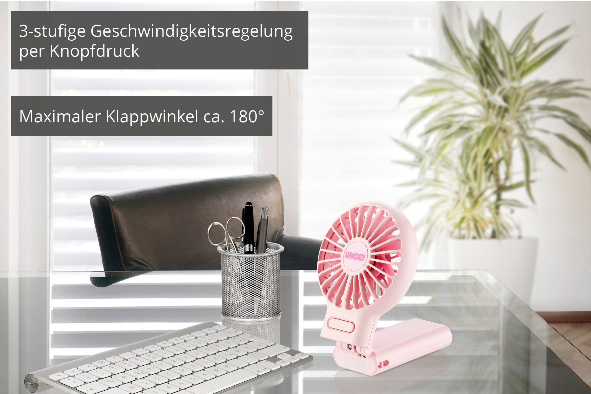 Ein rosafarbener Klappventilator steht auf einem Glastisch neben einer Tastatur.