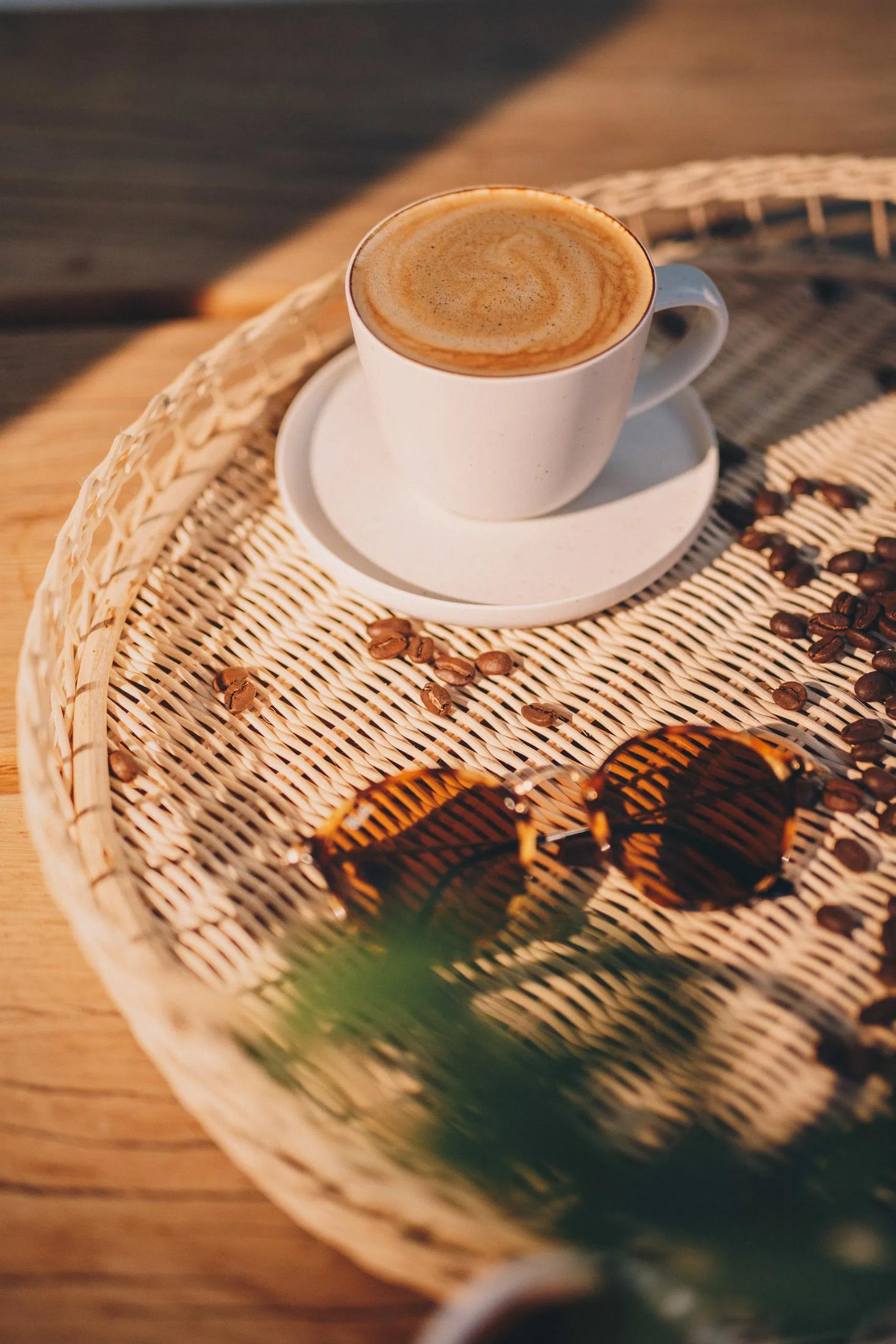 Kawa, ziarna kawy i okulary przeciwsłoneczne na plecionej tacy.