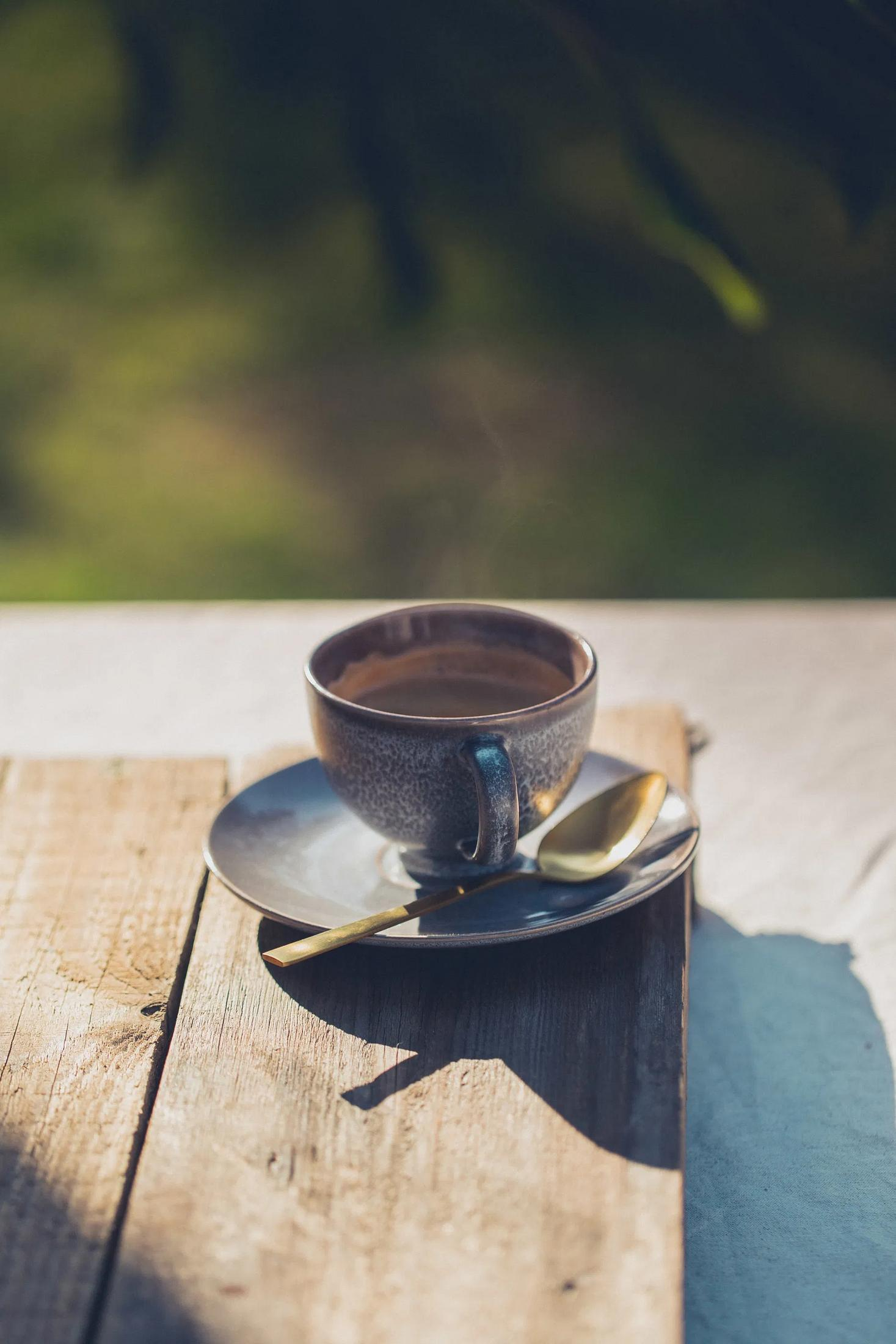 Parująca filiżanka kawy na spodku z łyżeczką na drewnie.