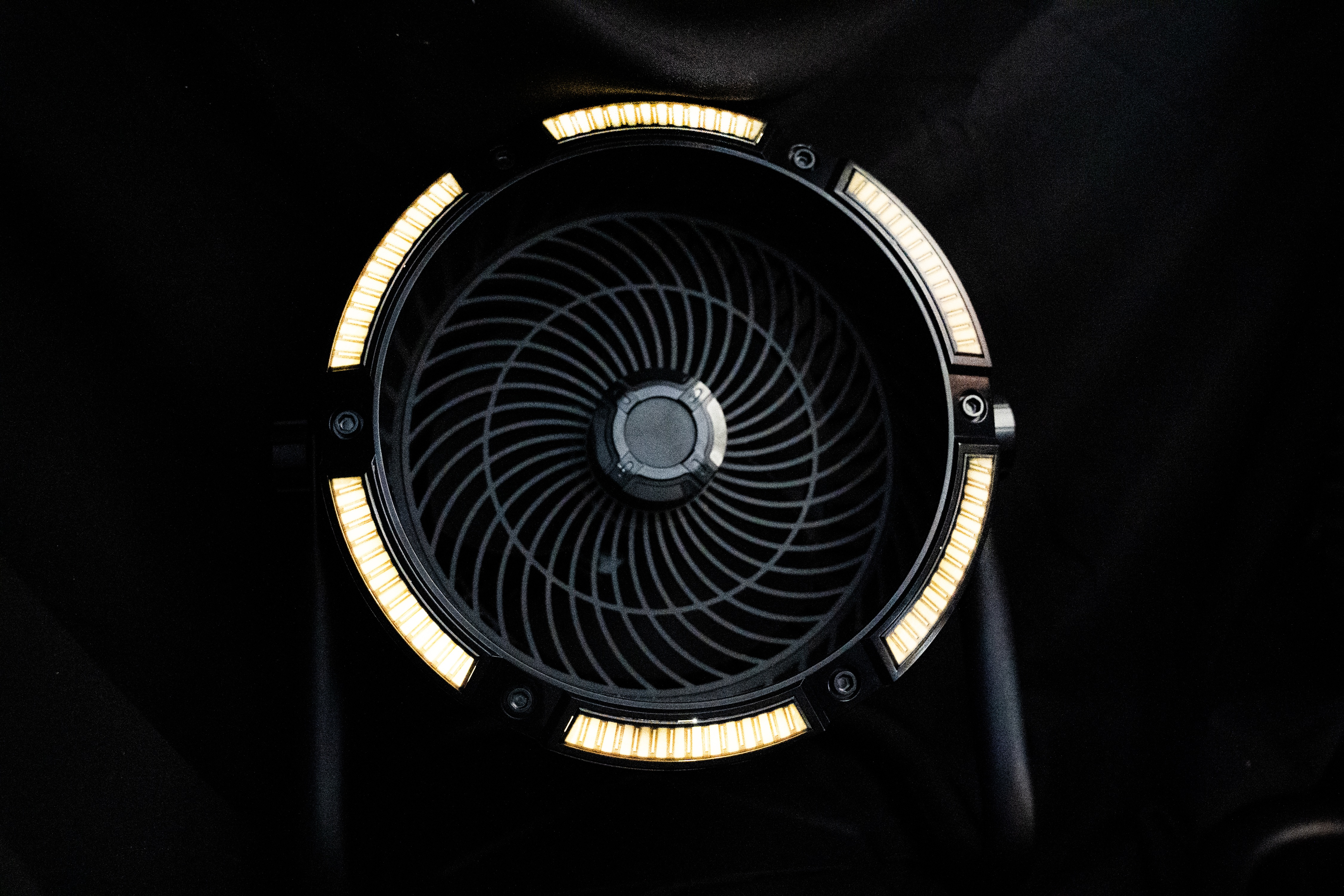 Ein dunkler Ventilator mit goldenen Lichtern am Rand auf schwarzem Hintergrund.