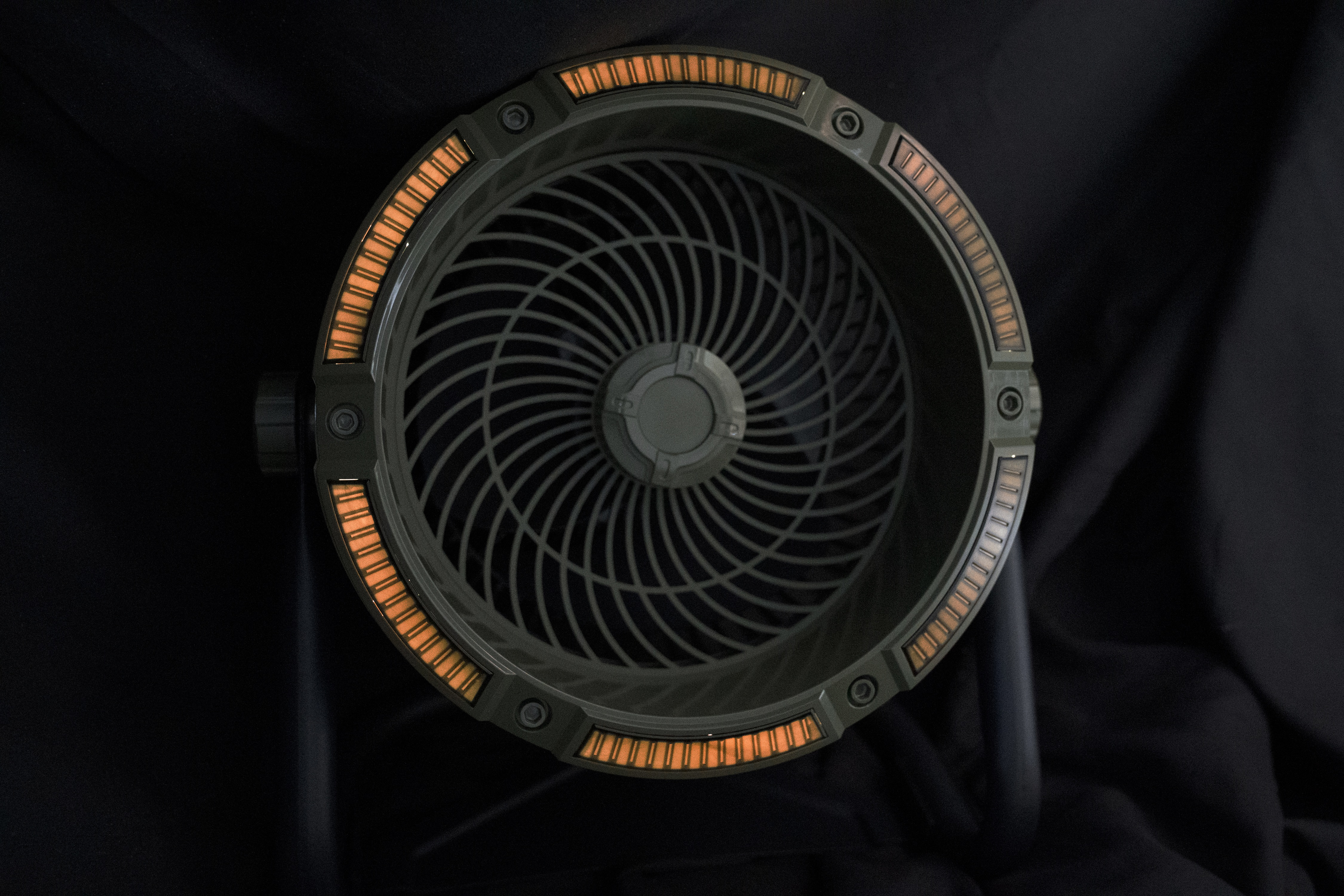 Okrągły, ciemnozielony wentylator z pomarańczowymi światłami na obrzeżu.