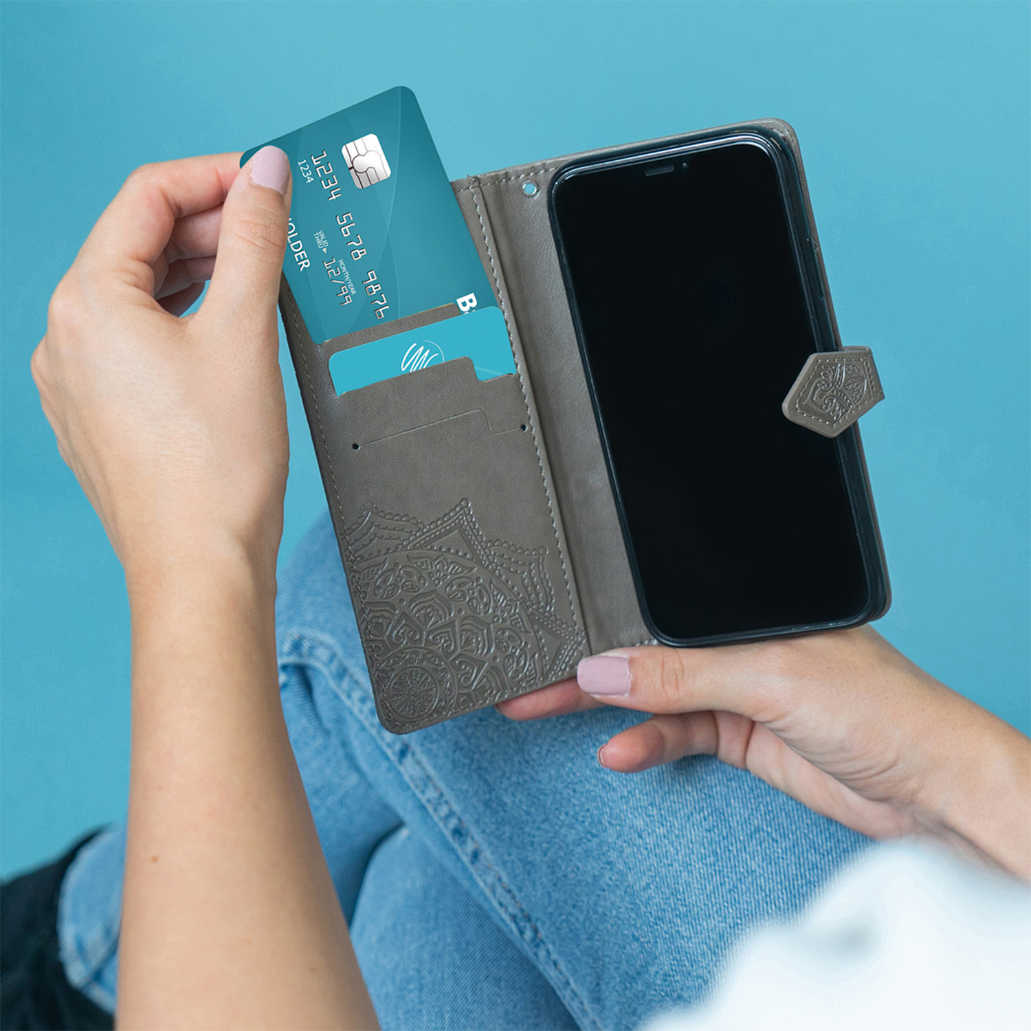 Een hand steekt een creditcard in een bruine portemonnee naast een smartphone.