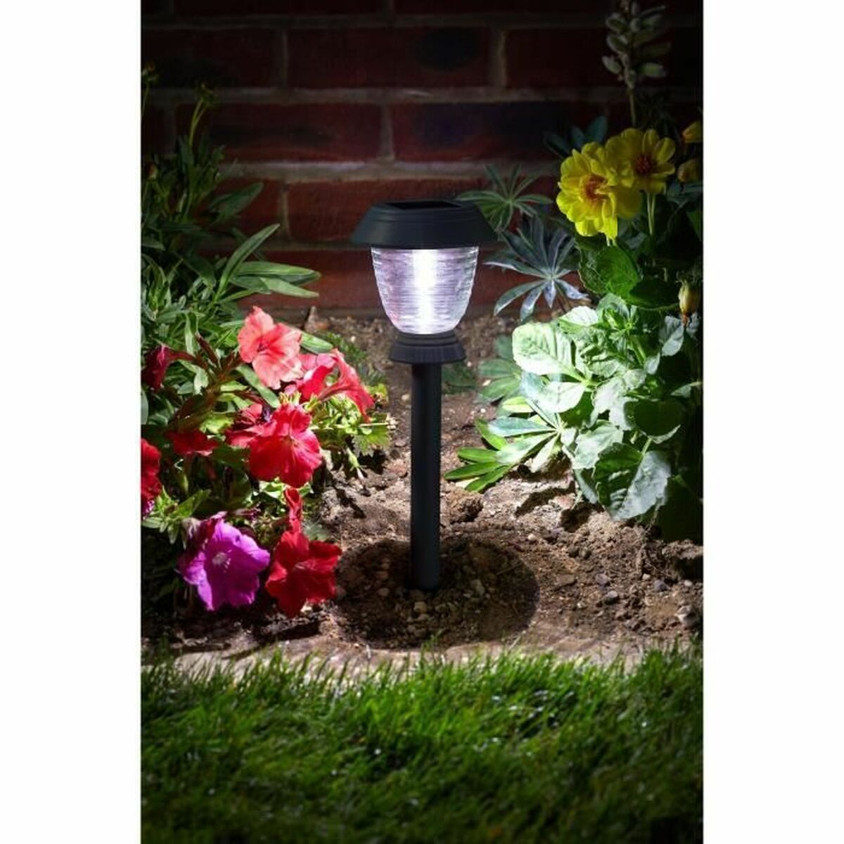 Eine Solarleuchte leuchtet in einem Blumenbeet mit roten und gelben Blumen.